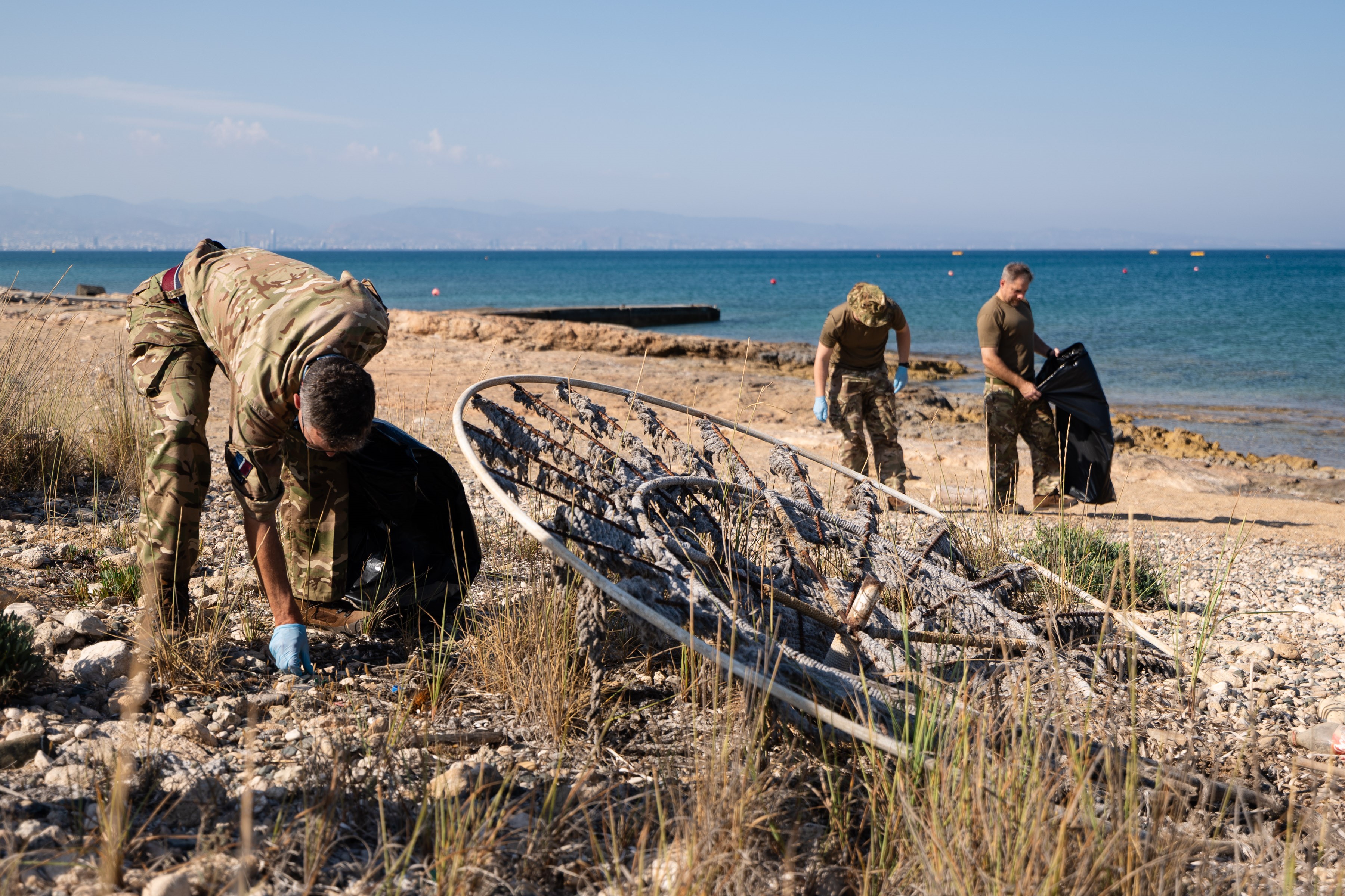 Servicepeople cleaning on the beach, wearing blue gloves and with binbags.