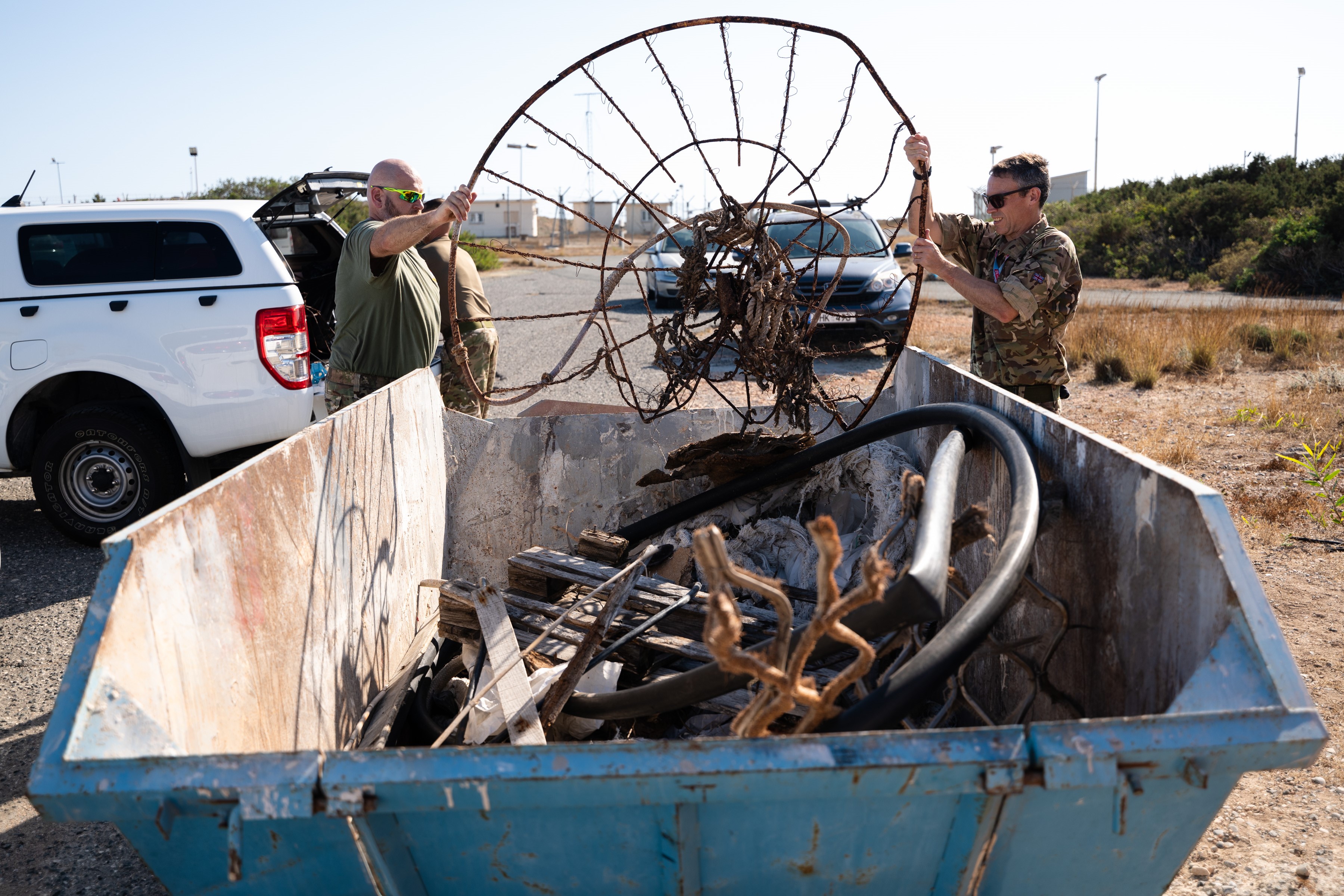 Two servicepeople putting rubbish into a skip.