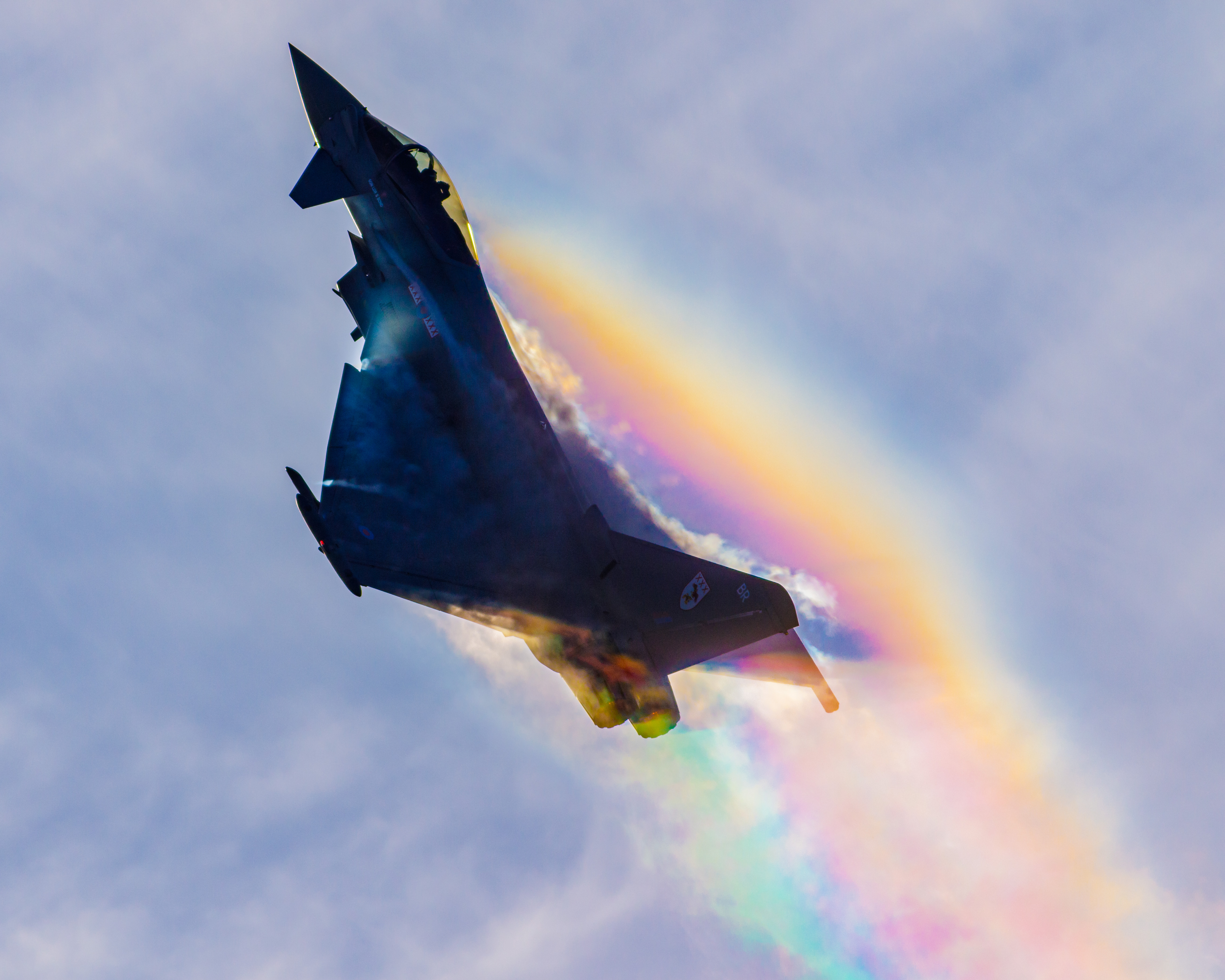 Photo of an RAF Typhoon flying almost vertically into the air, leaving behind a luminescent multicoloured trail.