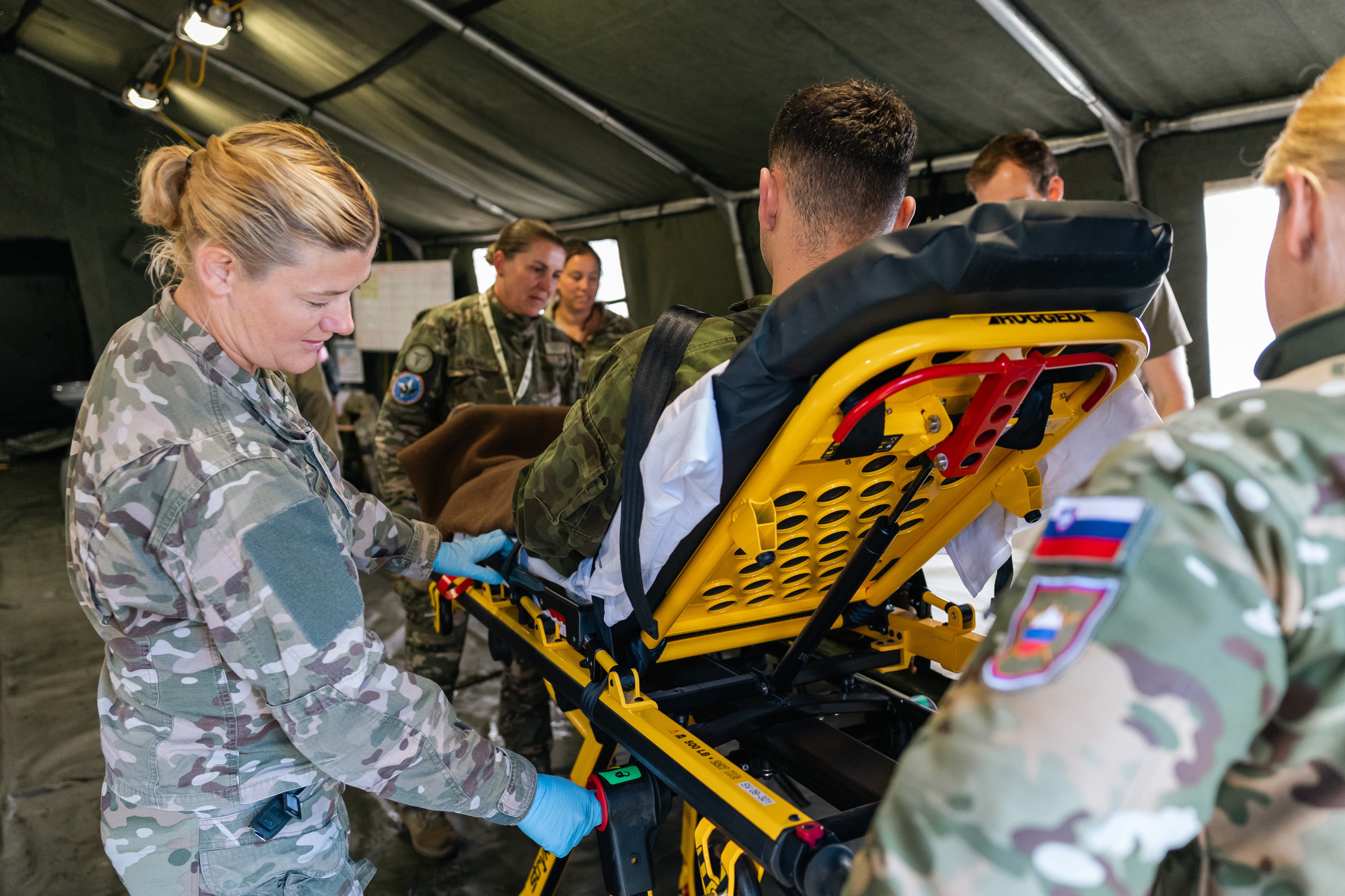 Various NATO personnel working to secure an "injured" actor into a medical trolley safely. A member of the Slovenian armed forces can be seen in the foreground.