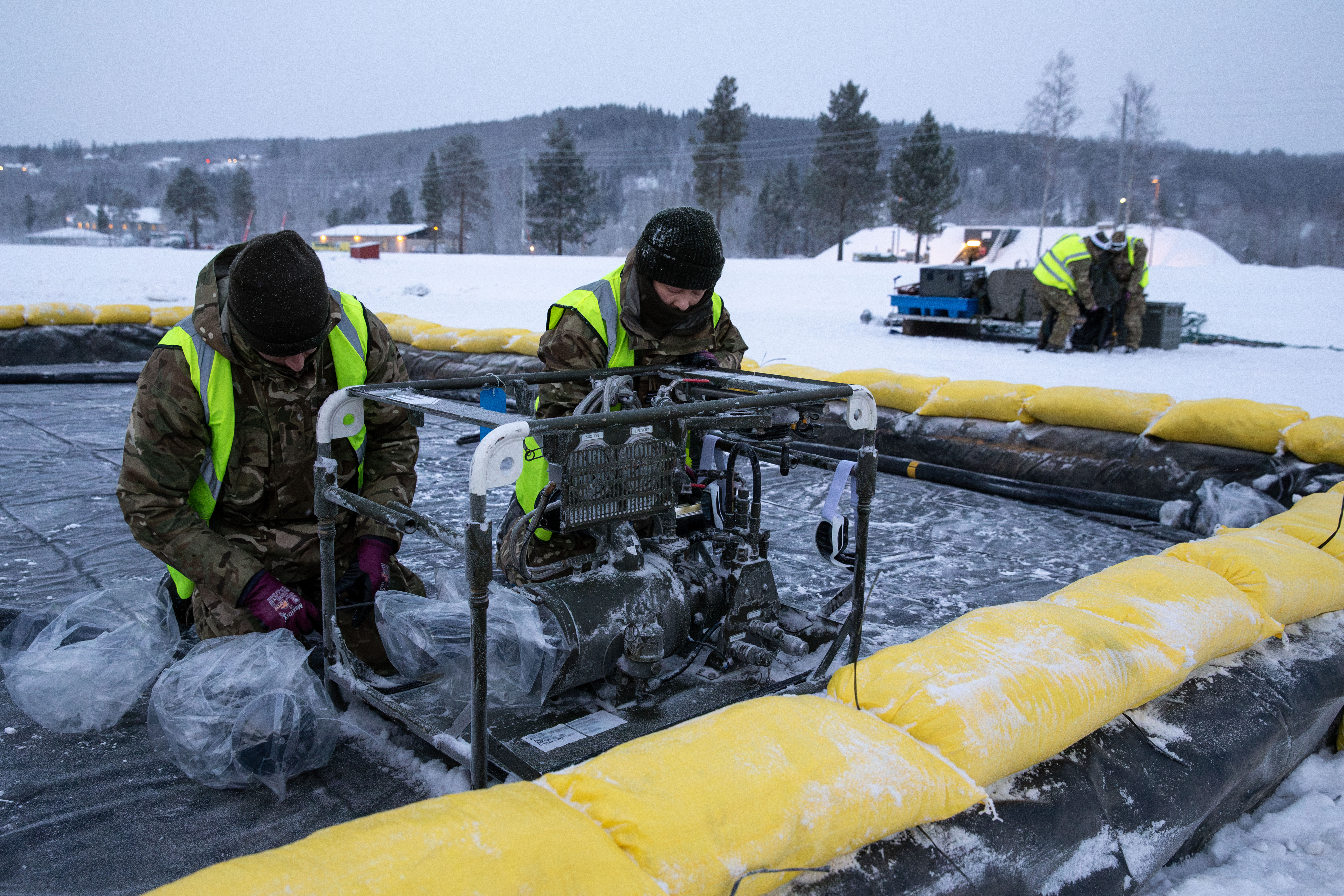 Two personnel with hi-vis on working on equipment outdoors in the snow.
