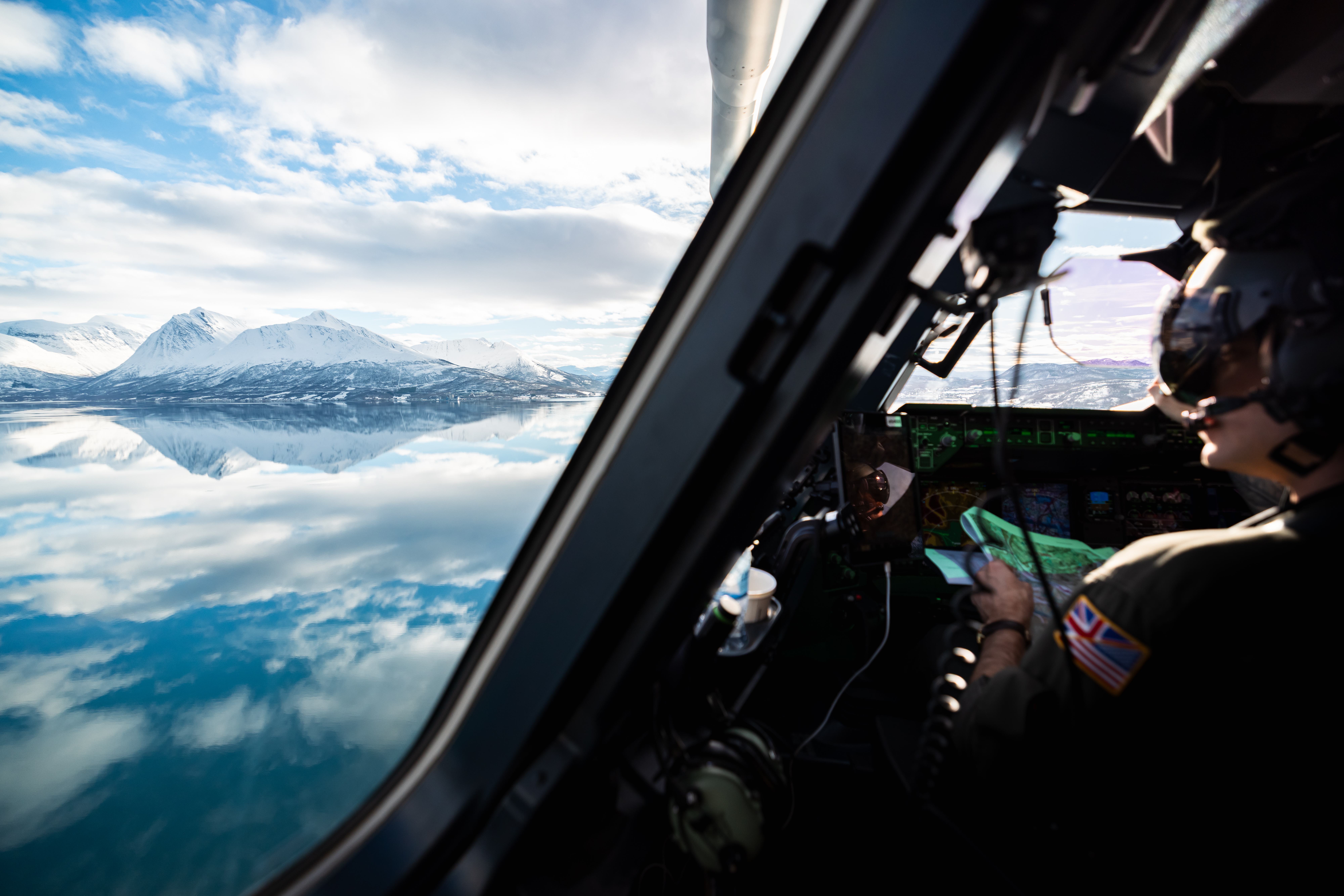 Photo of an RAF pilot looking out of an aircraft window towards a snowy mountain.
