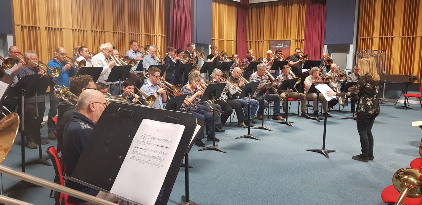 A woman conducts a large trombone ensemble.