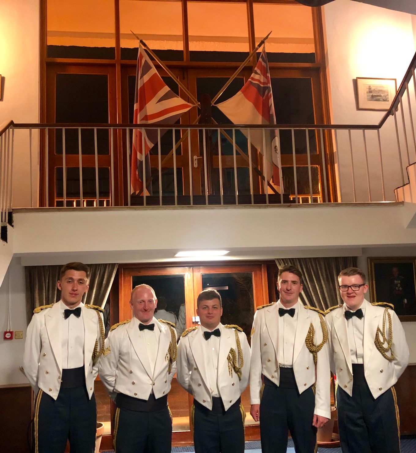 Five uniformed men pose for a photograph with flags behind.