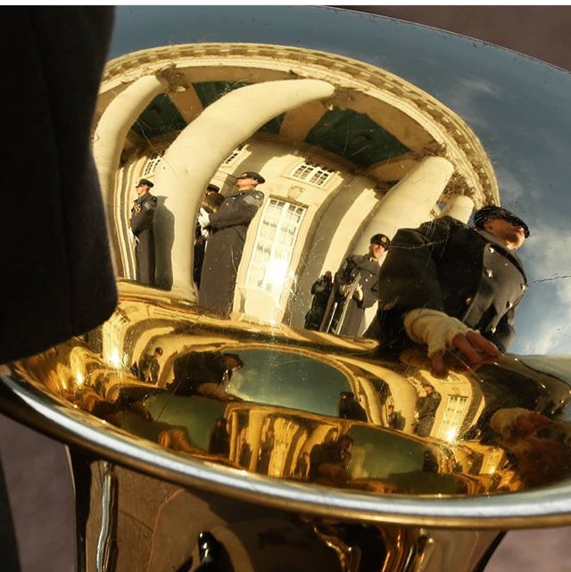 The bell of a tuba with people reflected in the shine.