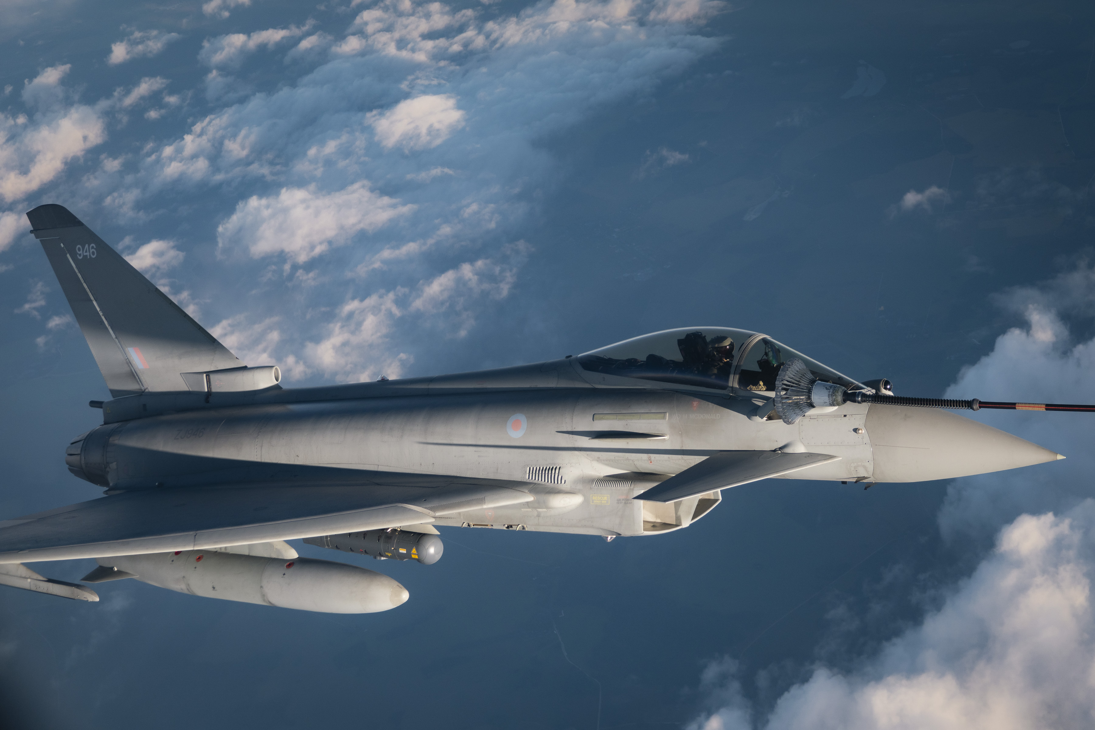 An RAF Typhoon being refuelled in the air over cloudy blue skies.