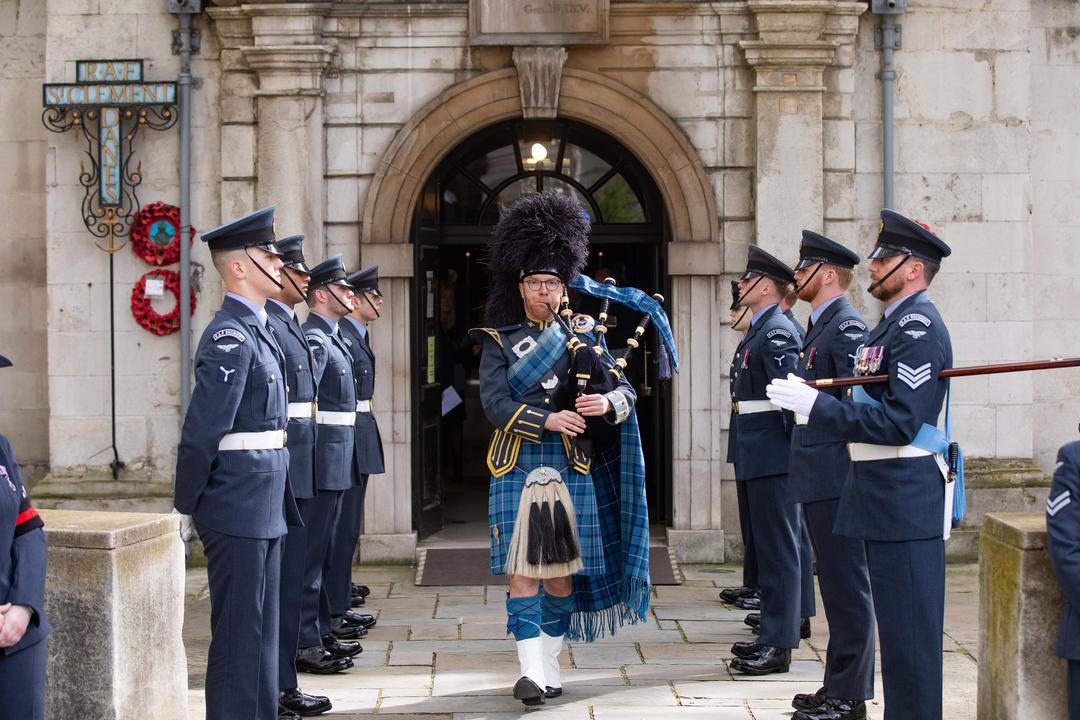 Bagpiper walking out of the church with personnel standing to either side