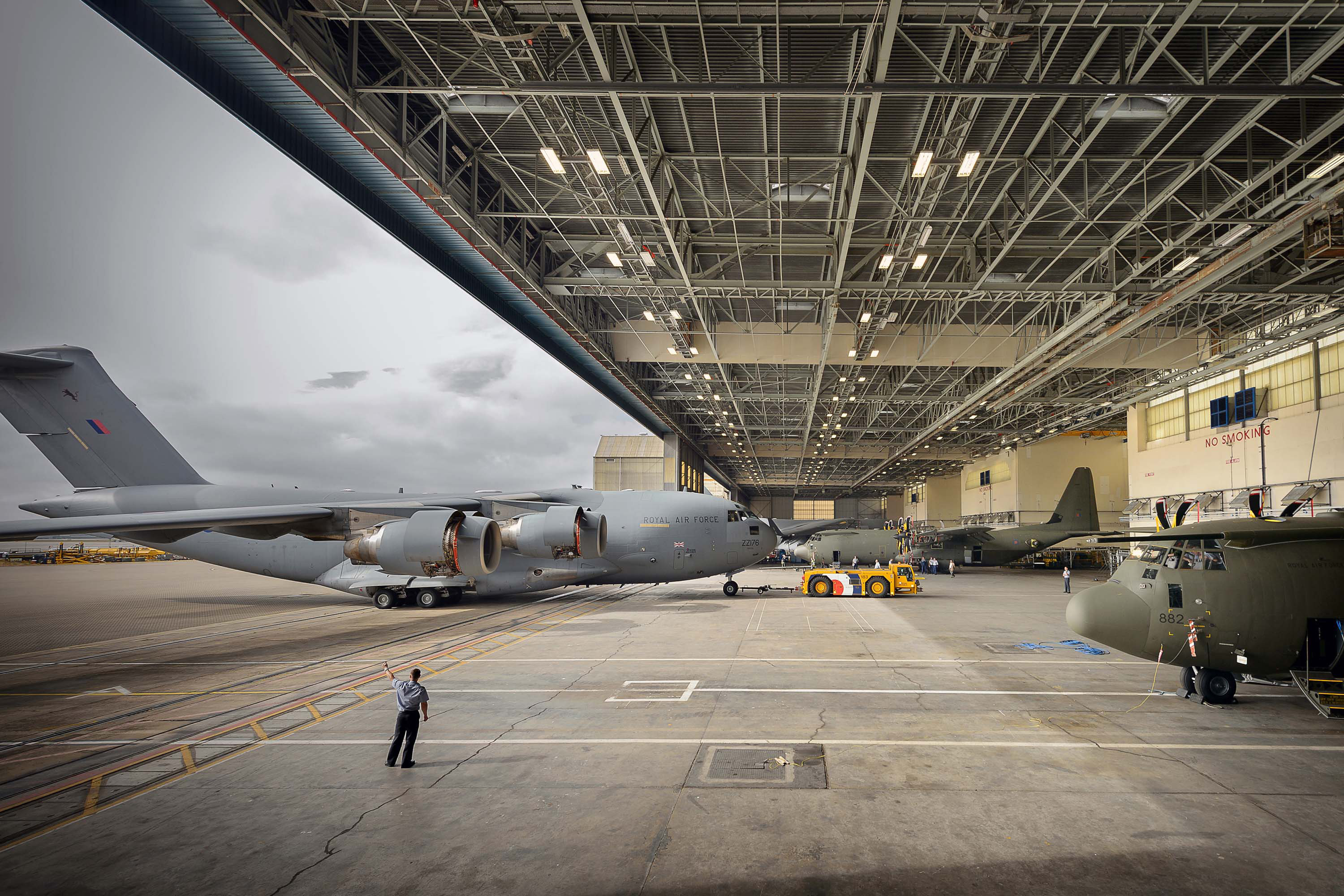An RAF Globemaster taxiing into a hangar at RAF Brize Norton, with two retired Hercules aircraft also visible.