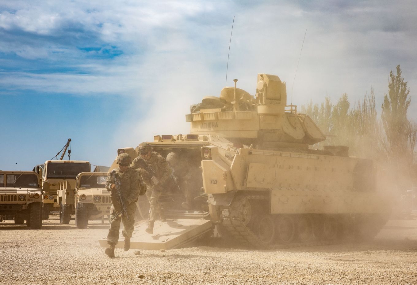 Personnel running out of their Bradley Infantry Fighting Vehicle with sand blowing. 