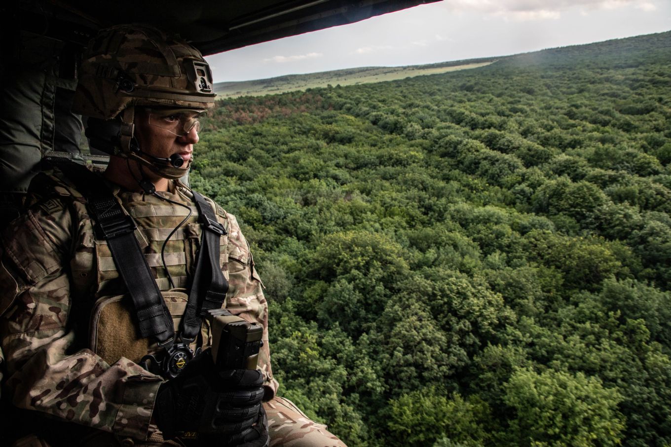 RAF Regiment Gunner looking out of a Hawk Helicopter over treetops.