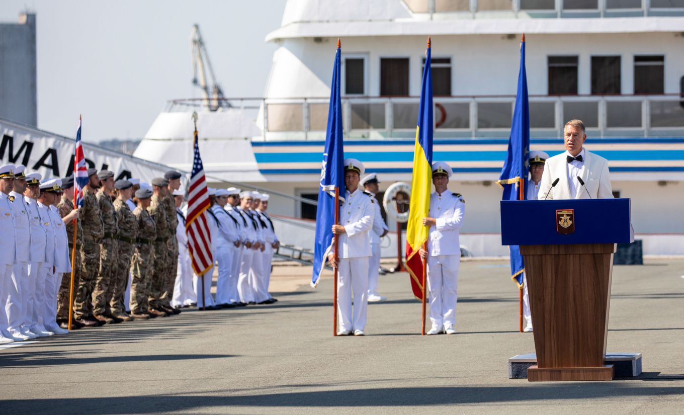 President of Romania at oration stand, with Navy and RAF personnel standing in parade with flags.