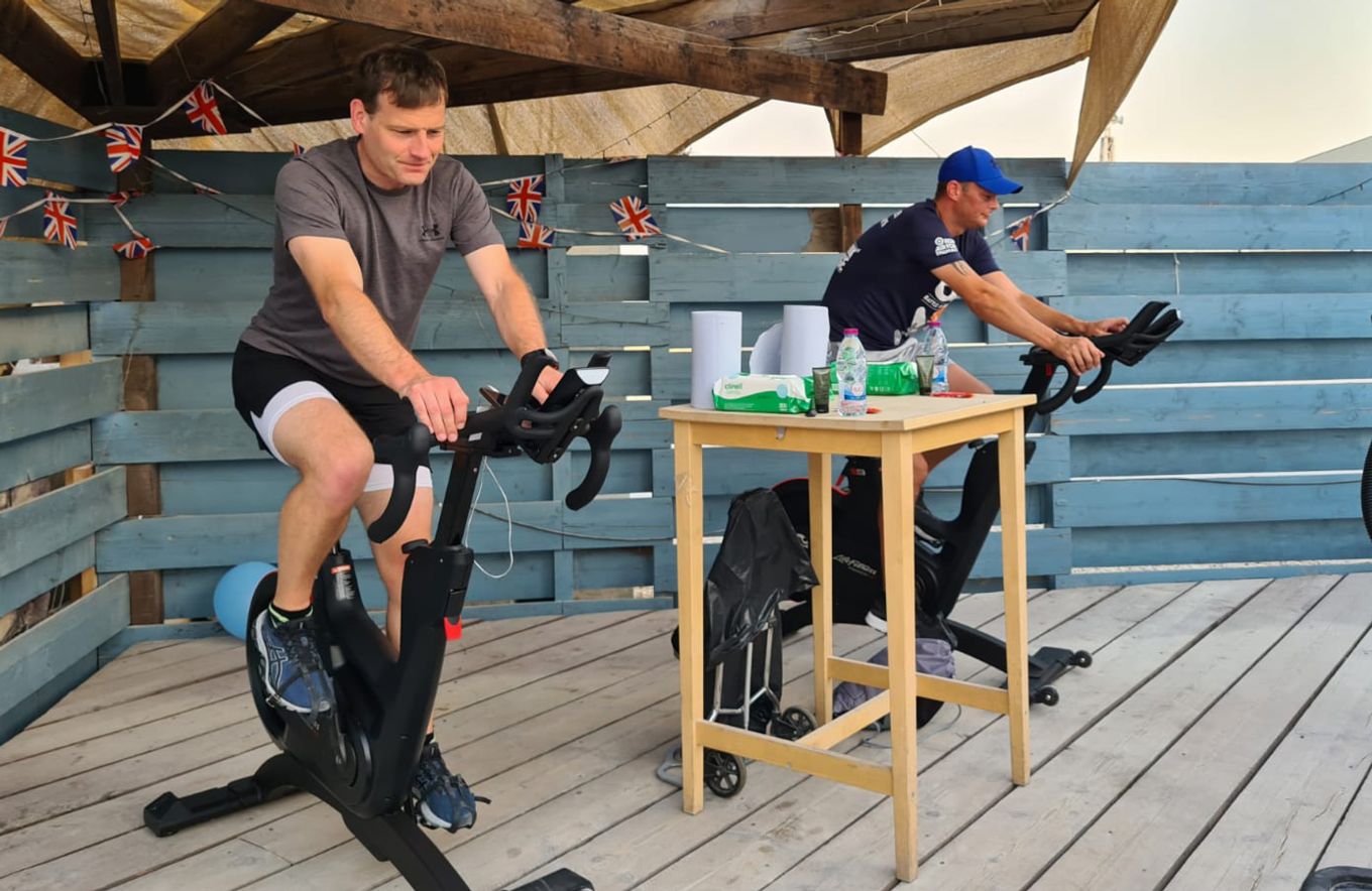 Two personnel on exercise bikes with hand sanitiser station between them.
