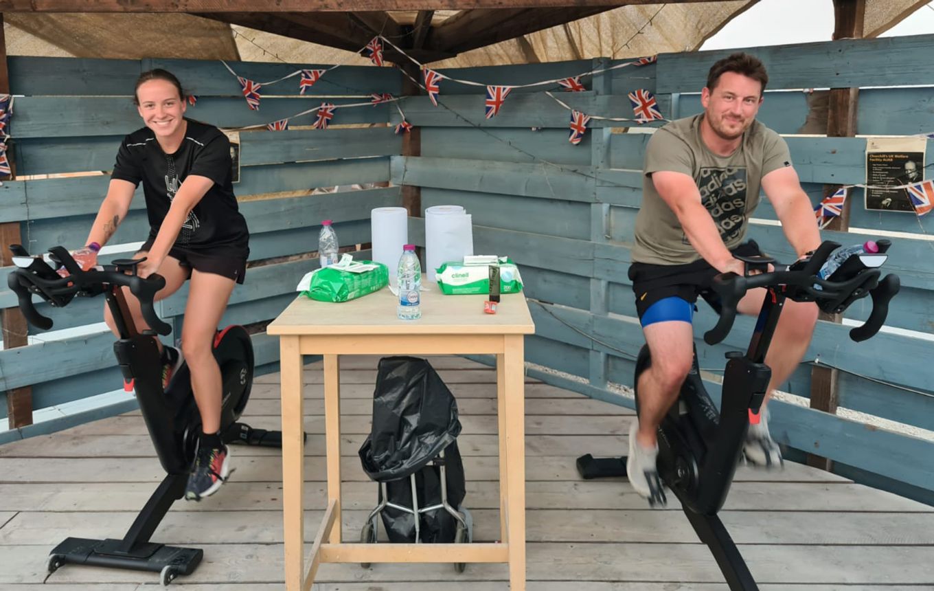 Two personnel on exercise bikes with hand sanitiser station between them.