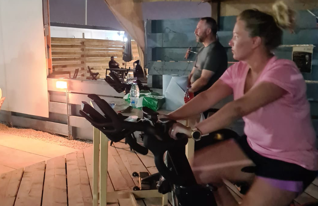 Two personnel on exercise bikes with hand sanitiser station between them.