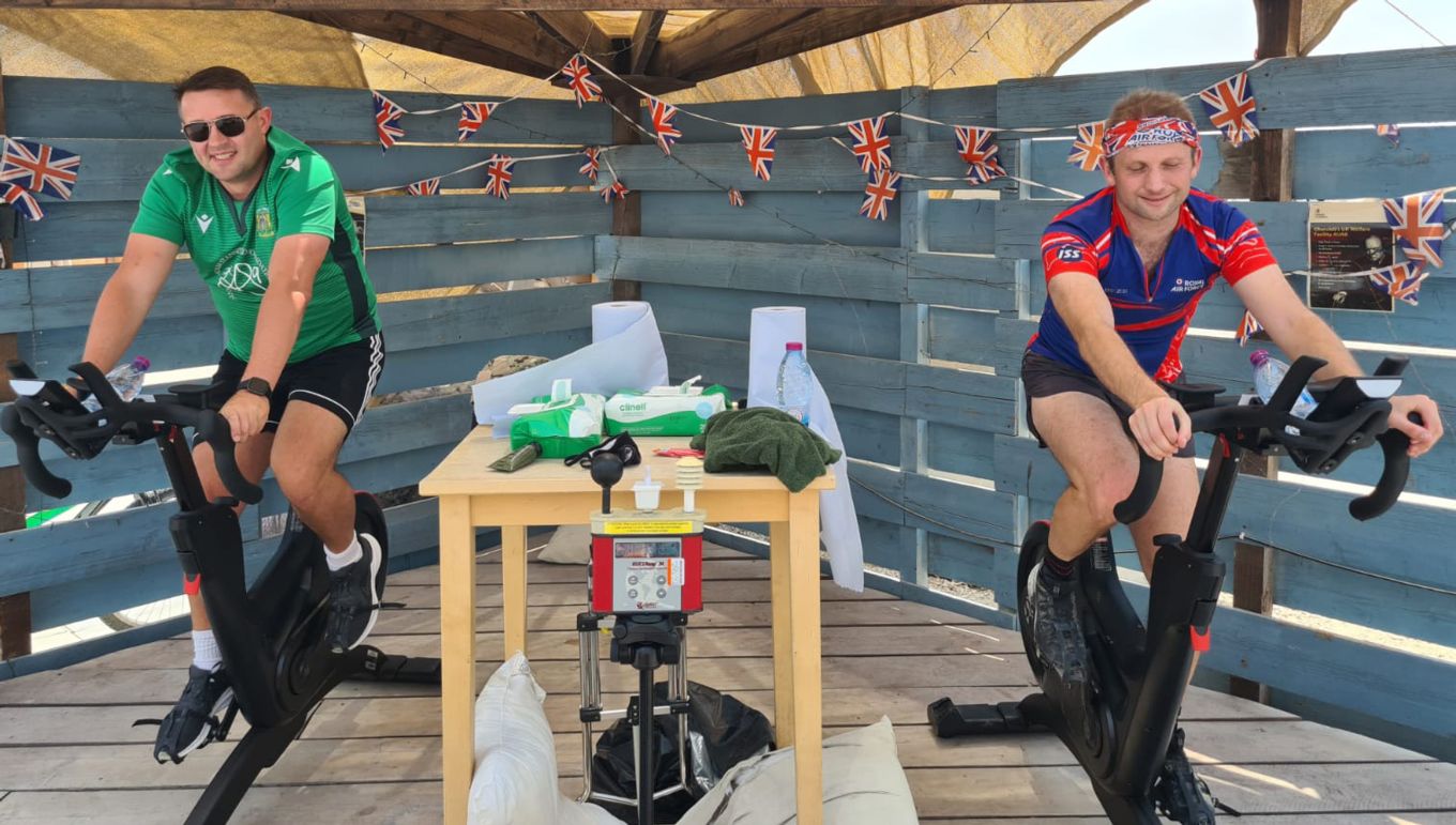 Two personnel on exercise bikes with hand sanitiser station between them.