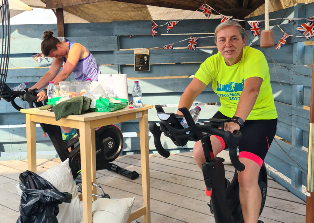 Two personnel on exercise bikes with hand sanitiser station between them.
