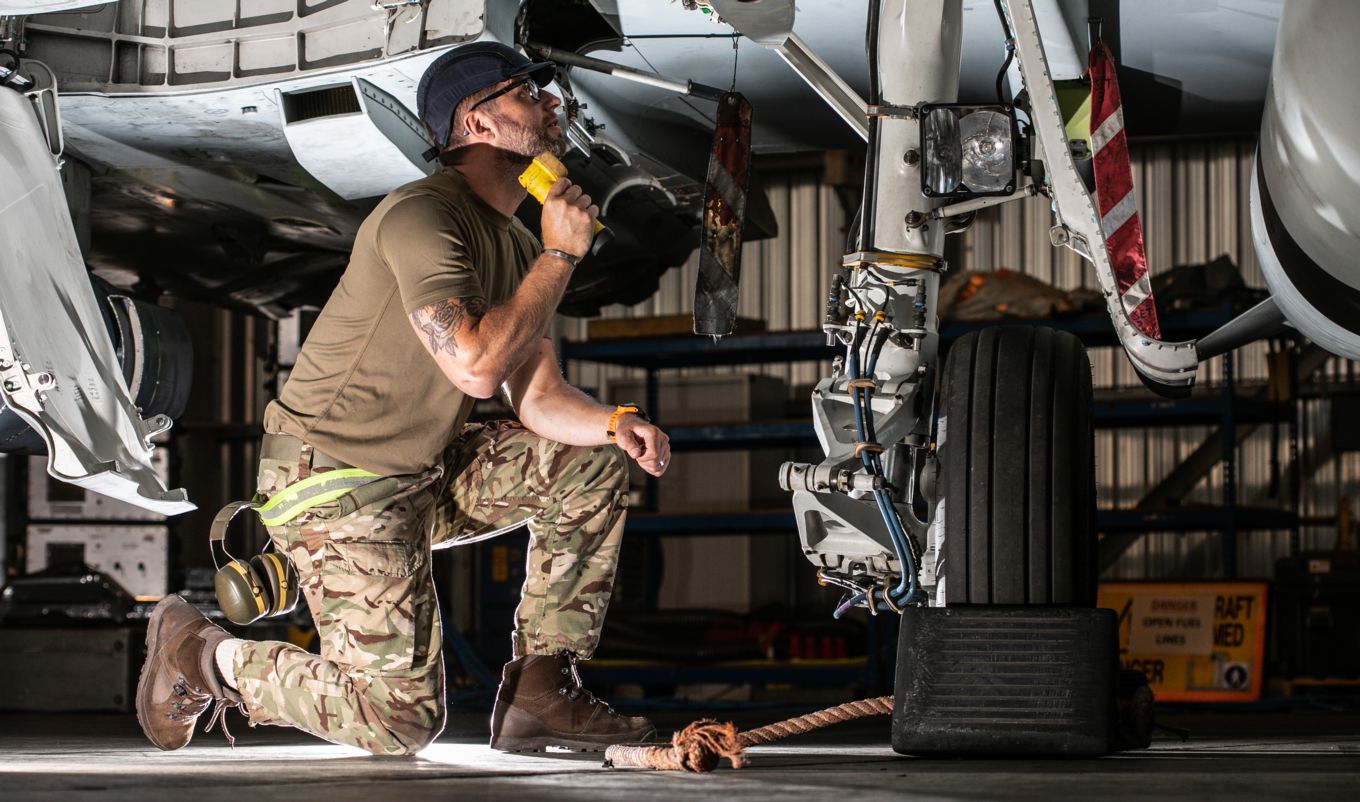 Member of 1(F) Squadron performs maintenance checks on the wheel of a Typhoon, holding a torch.