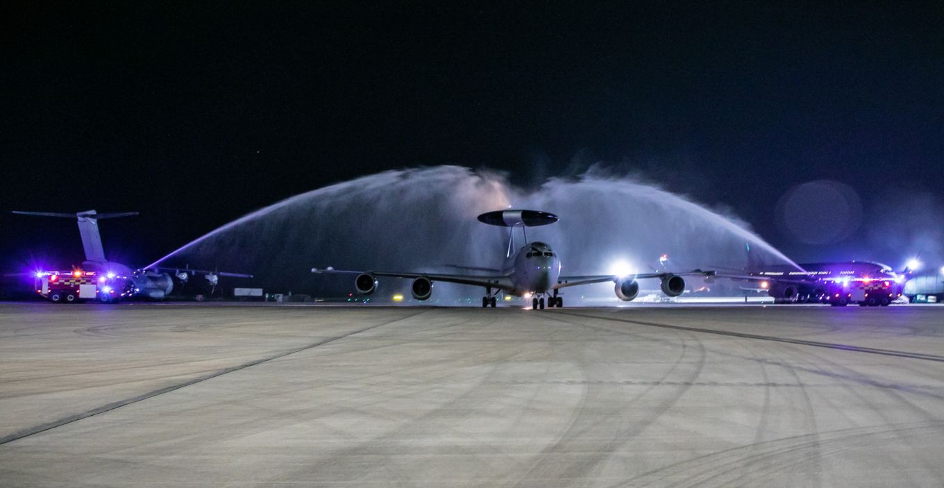 E-3D Sentry on the runway with water arch from emergency vehicles at night.