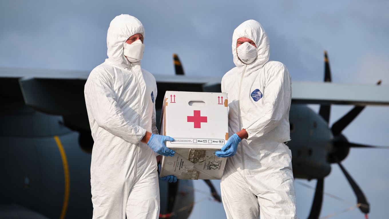 Image shows two people wearing protective clothing carrying medical supplies.