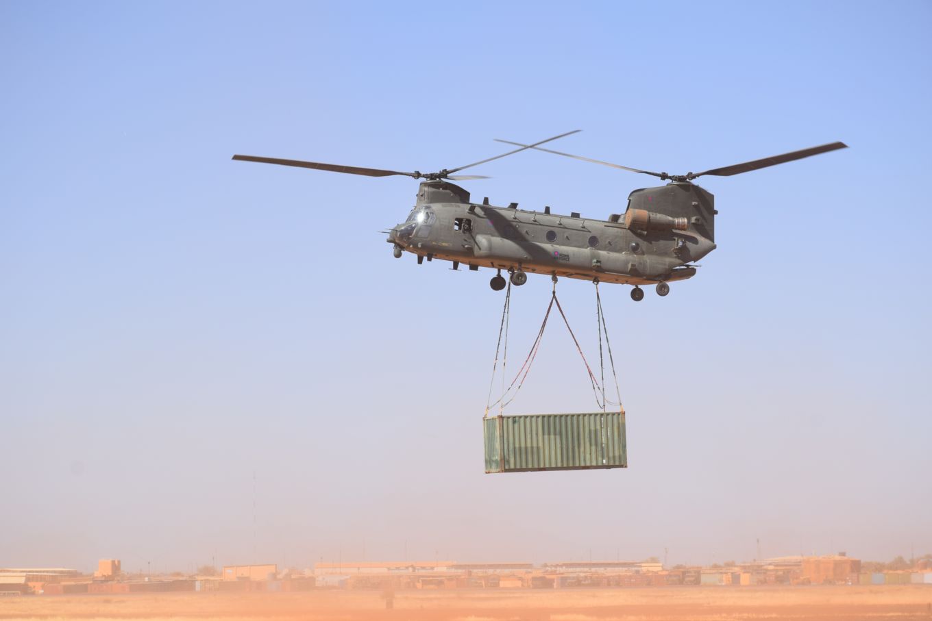 Image shows RAF Chinook in the desert with container hanging below.