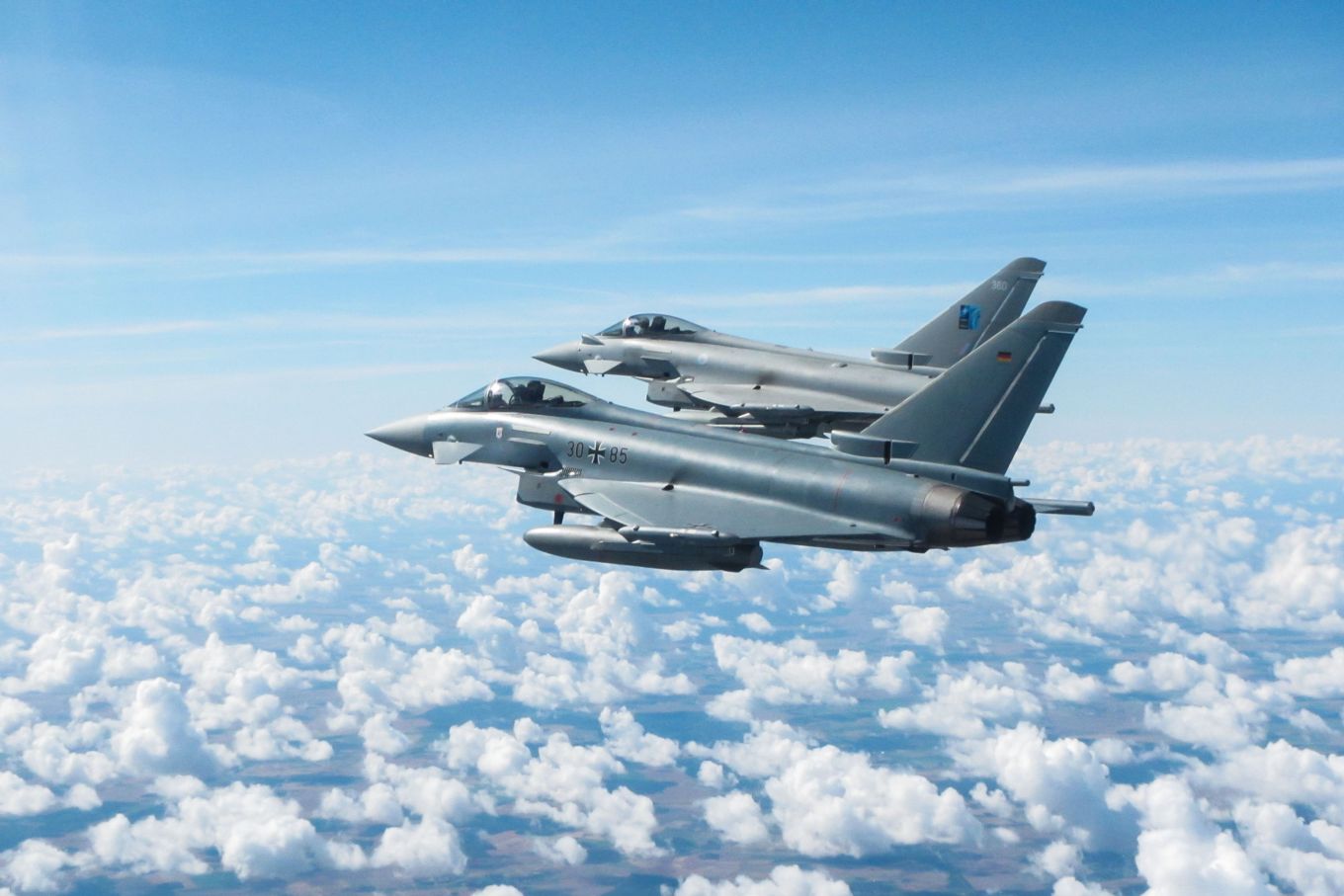 Image shows an RAF Typhoon flying above clouds next to a German Eurofighter aircraft.