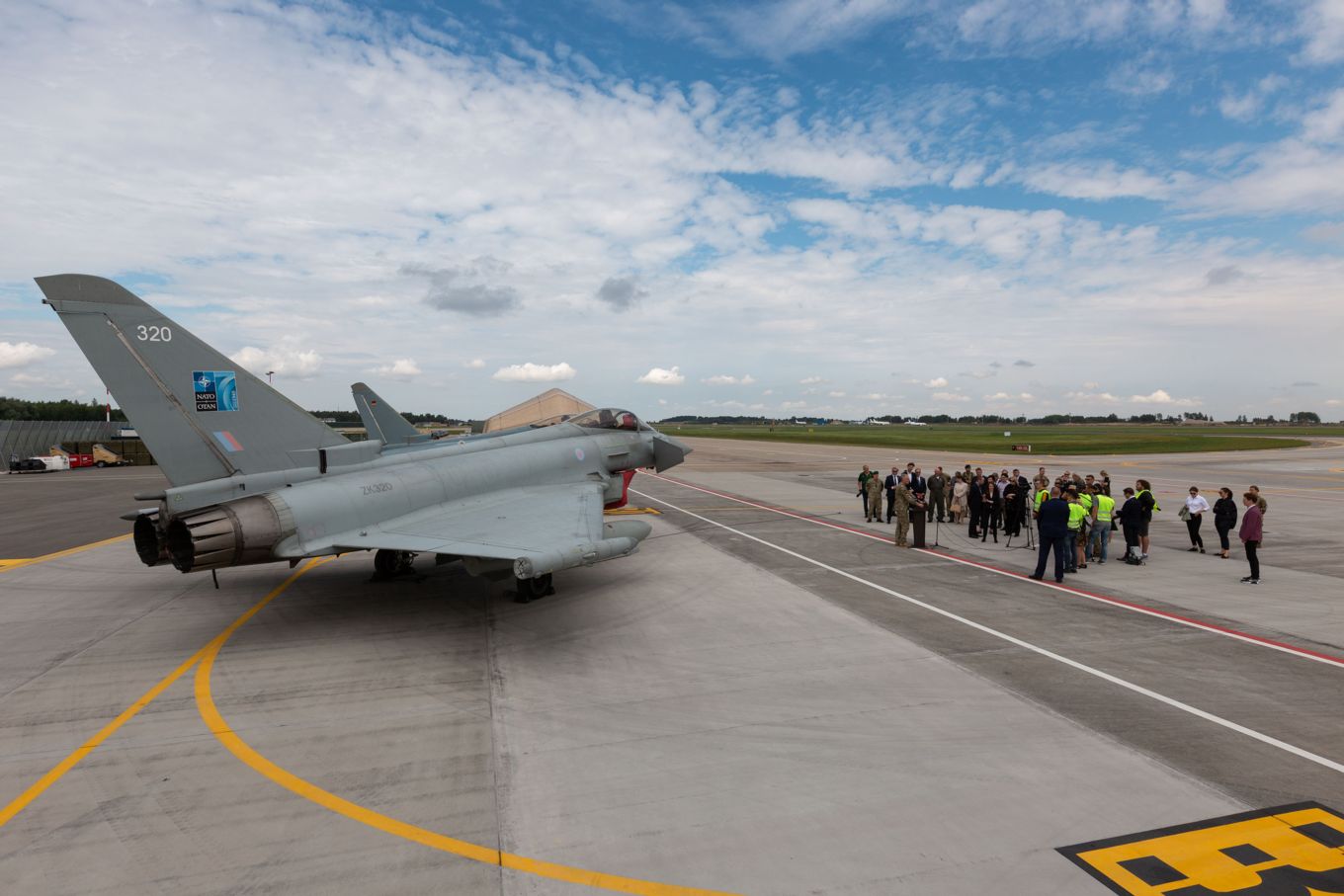 Image shows an RAF Typhoon on the tarmac with people gathered round a person speaking a at a podium.