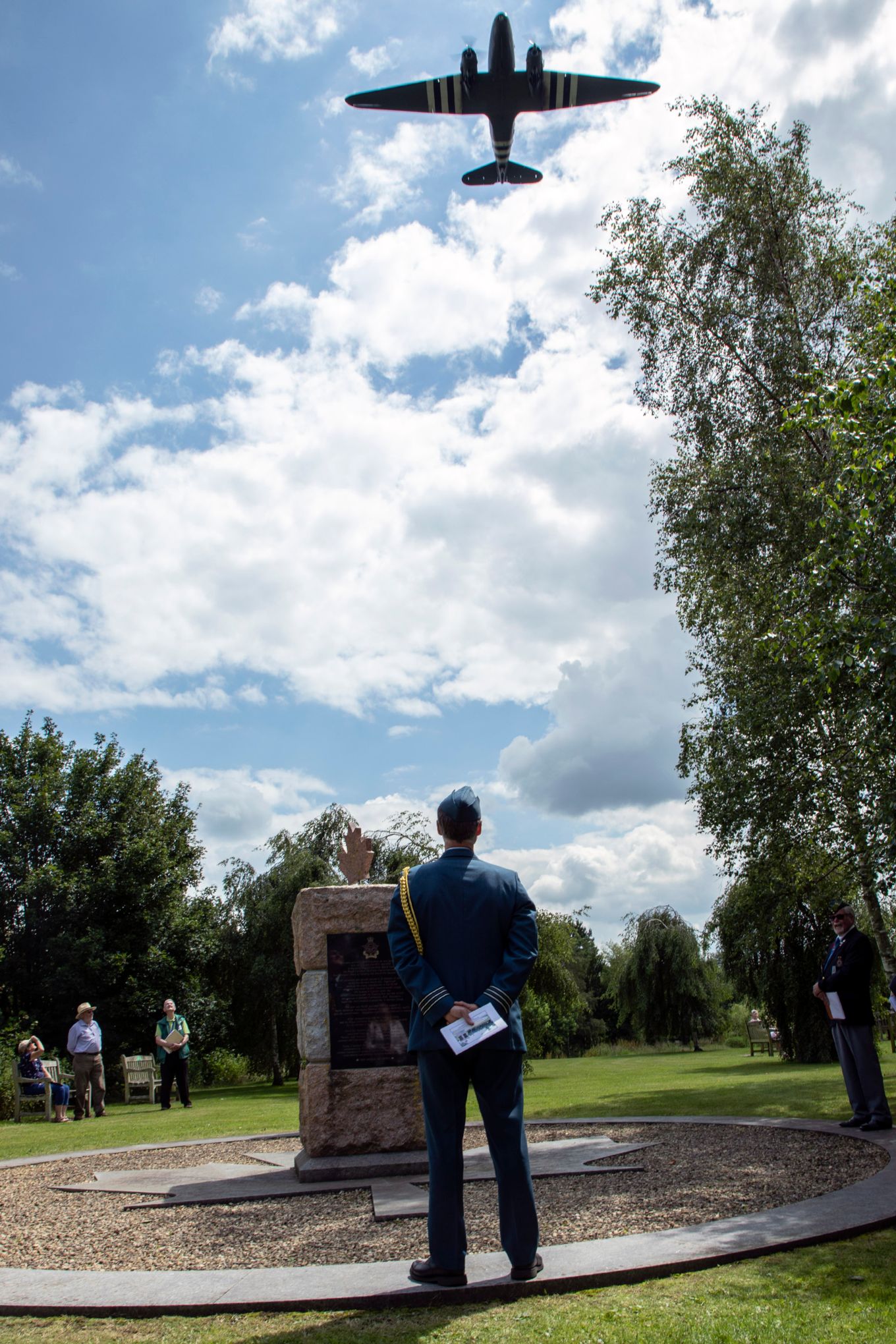 Personnel stands by Memorial, plane flypast overhead.