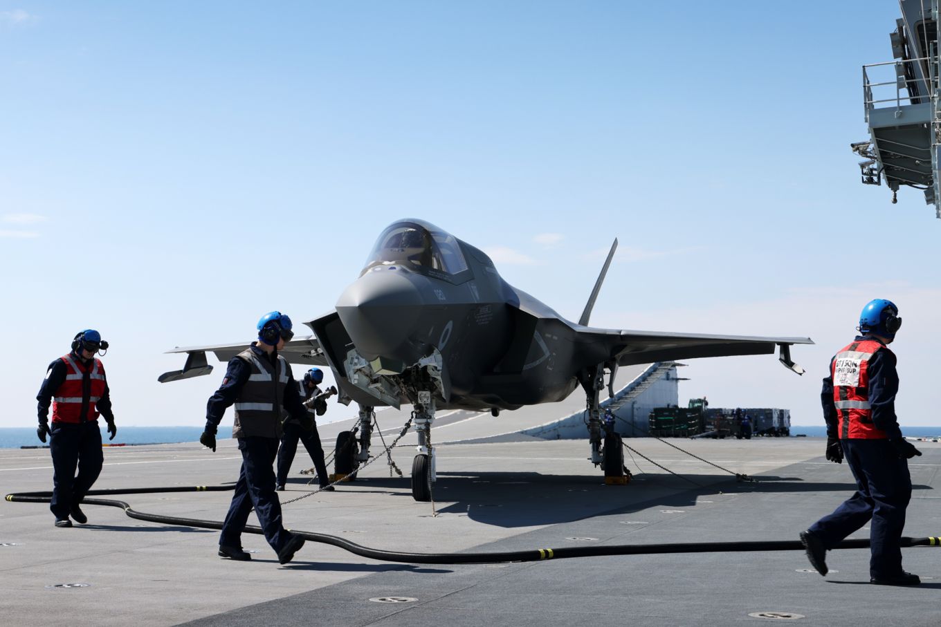 Three men walk round a landed F-35B Lightning Jet, refueling and checking maintenance.
