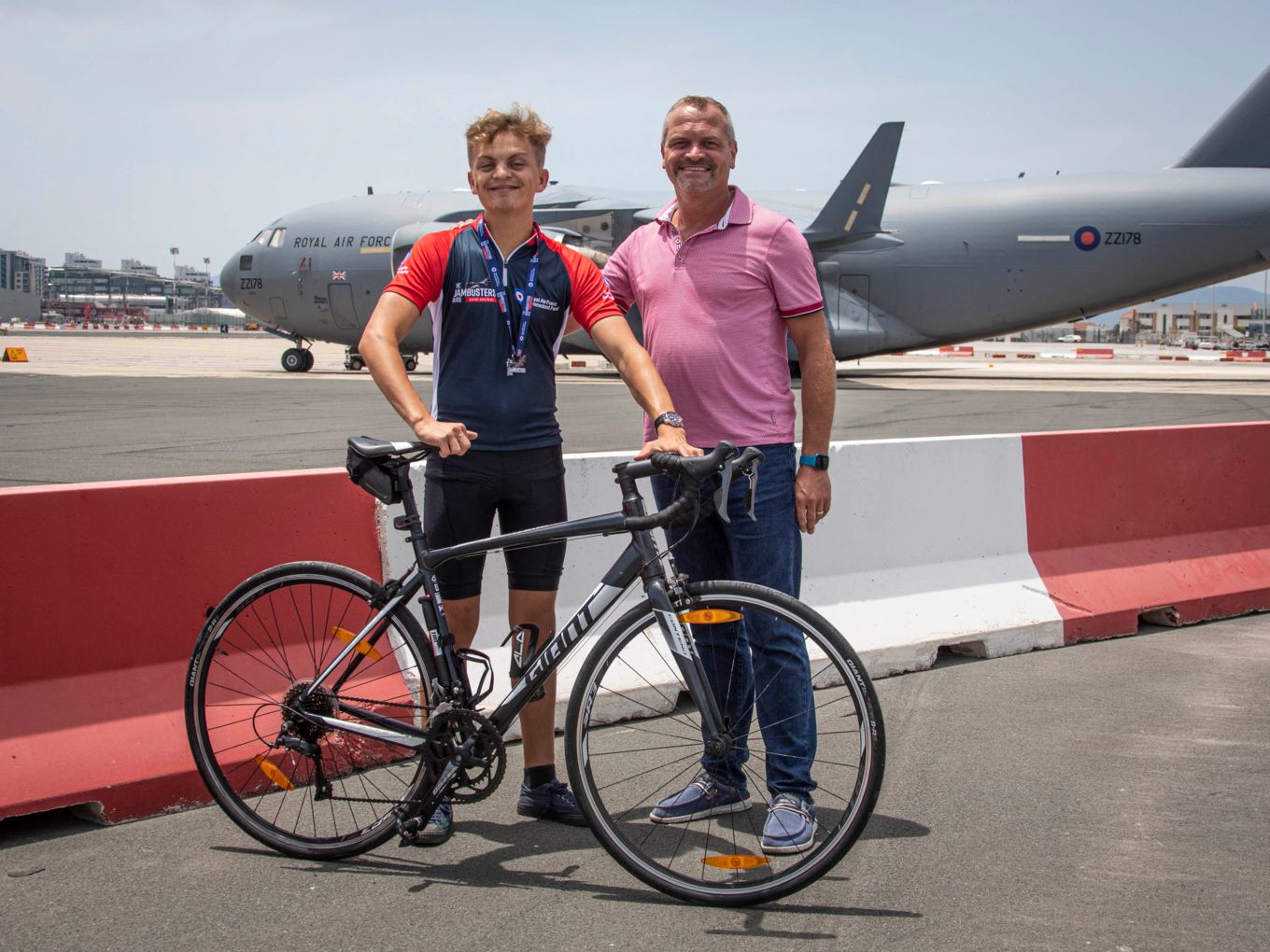 Oliver and his dad stand with his bicycle and a Globemaster in the background.