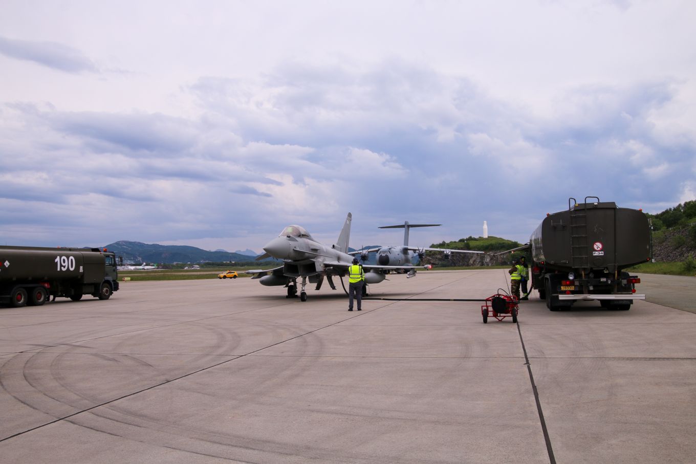 Typhoon aircraft being refuelled on the ground, with fuelling vehicles and A400M Atlas in the background.. 
