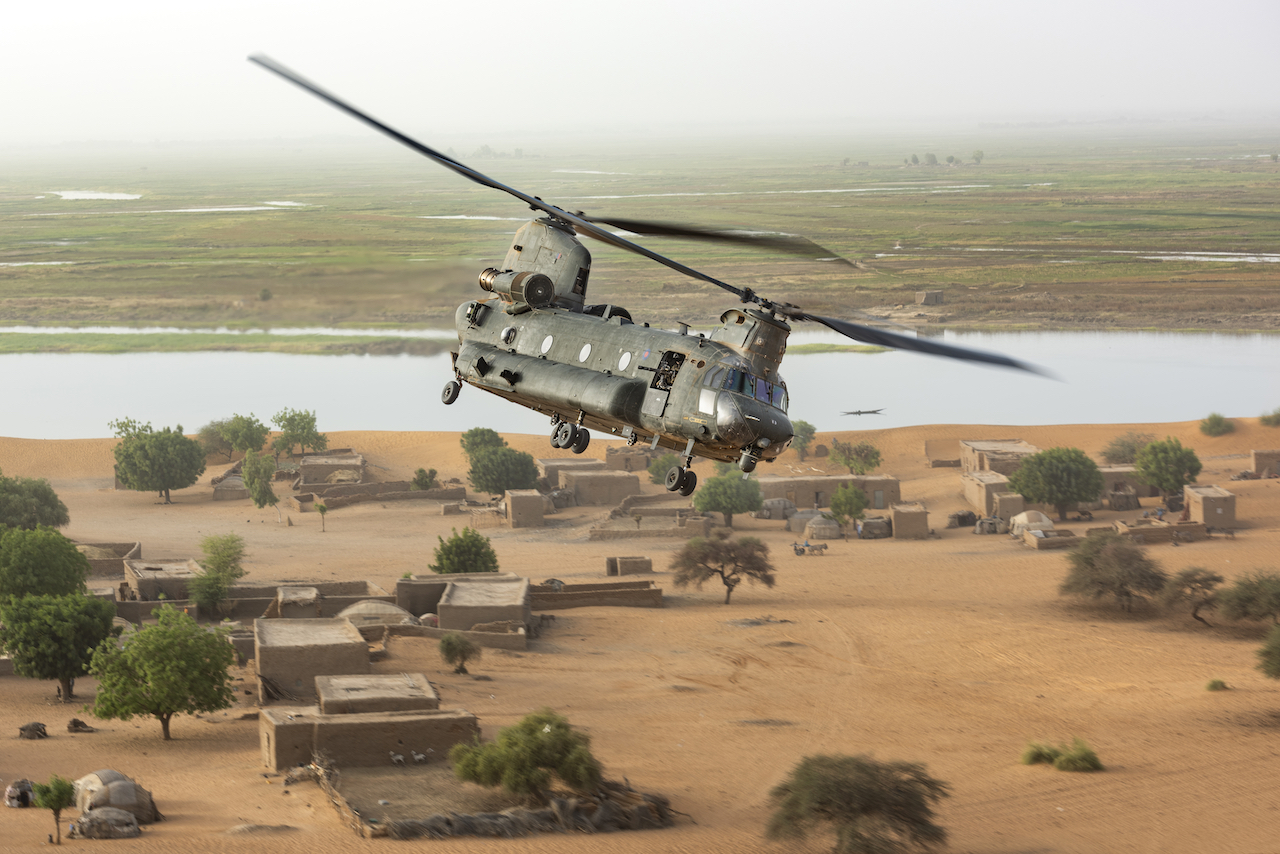 Chinook flies low over a town by the river, in Mali. 