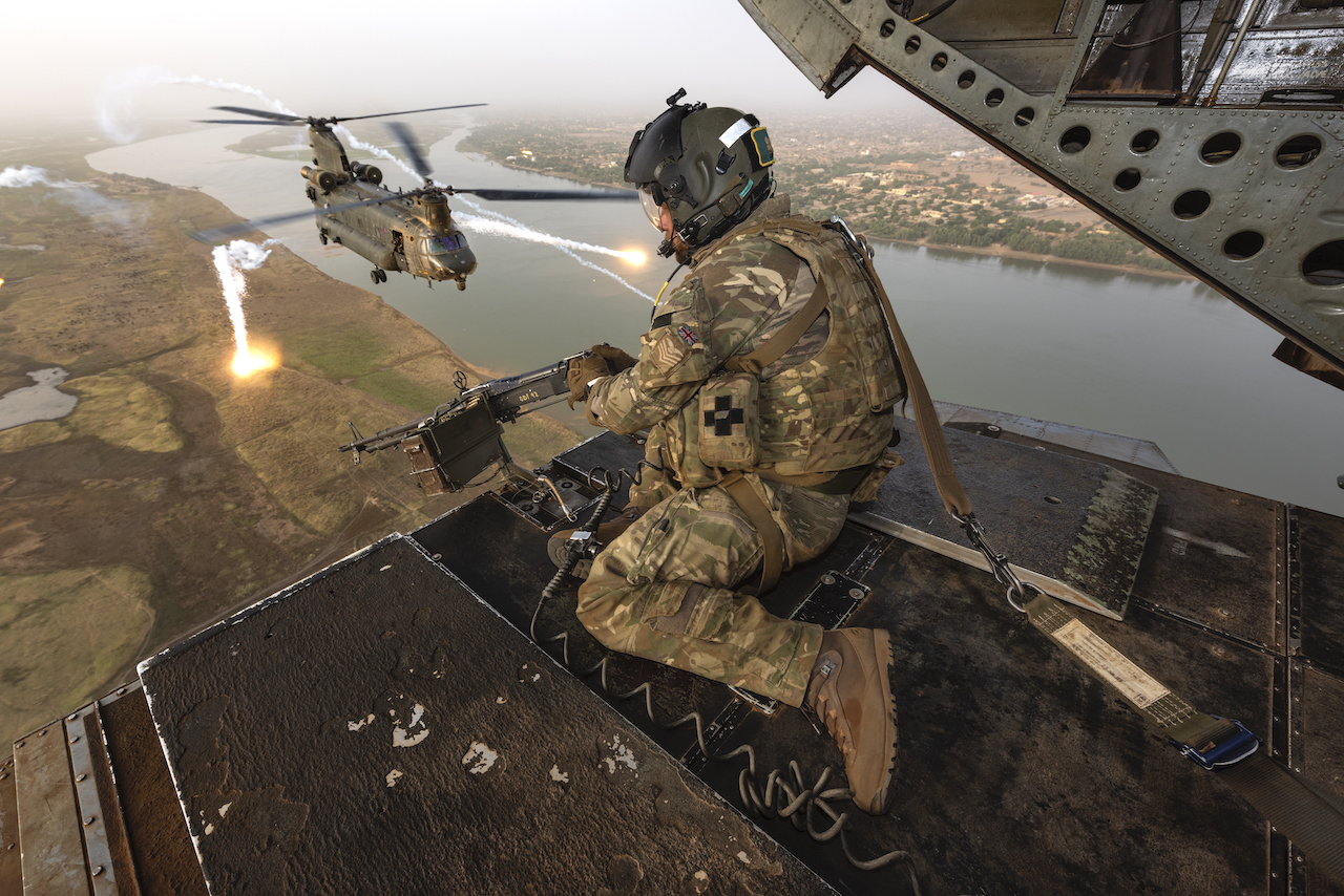 Gunner manning the rear door, followed by a Chinook flying between flares.