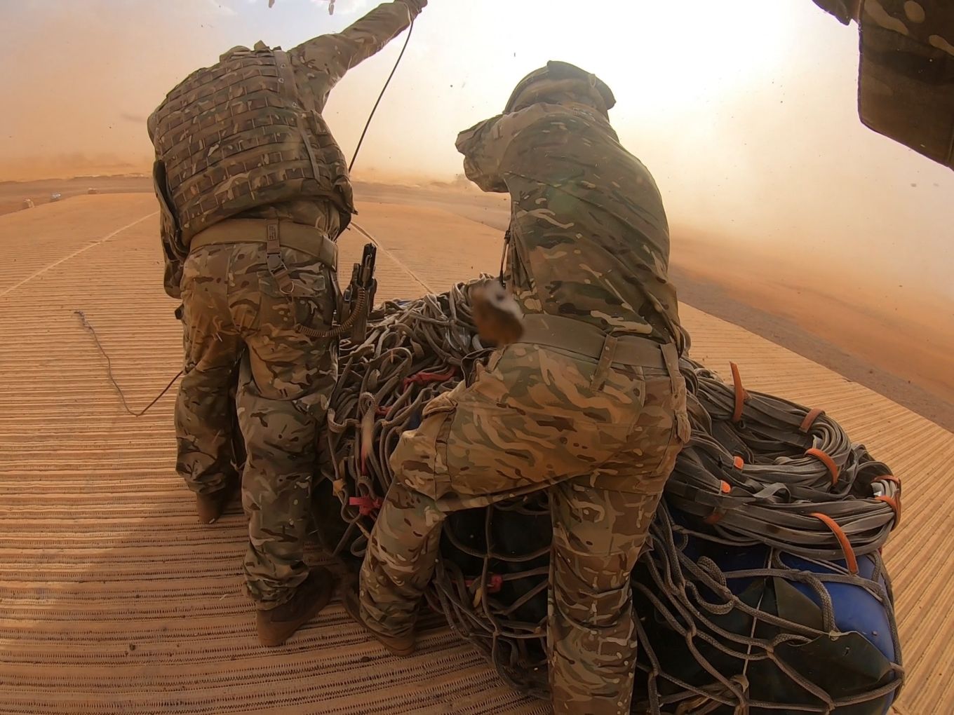 Personnel attach hooks to Chinook, as it hovers ahead and stirs up sand.