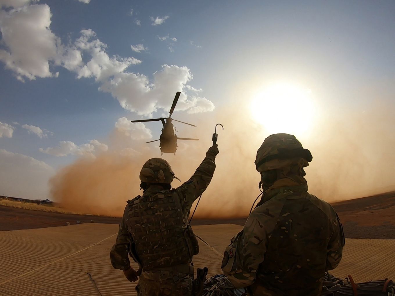 Personnel with hooks as Chinook hovers ahead and stirs up sand.