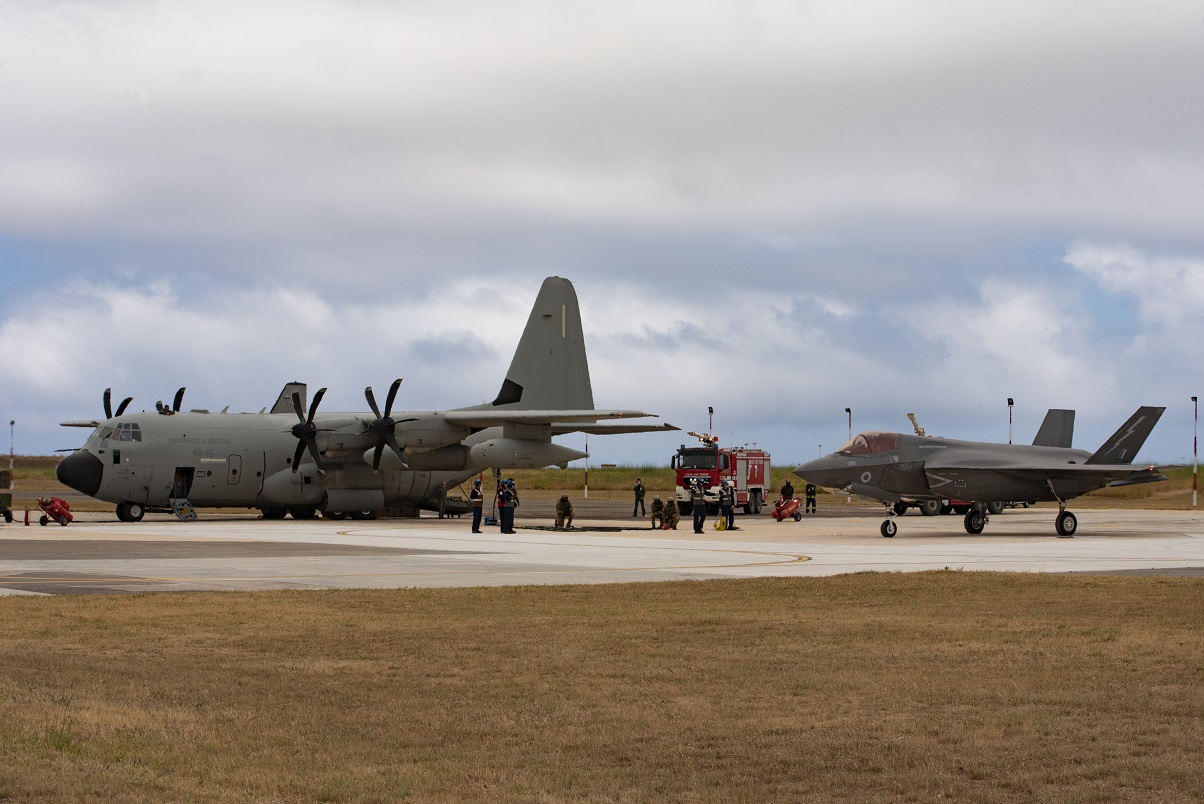 F-35B Lightning and KC-130J tanker on the ground, with personnel and a fire engine. 