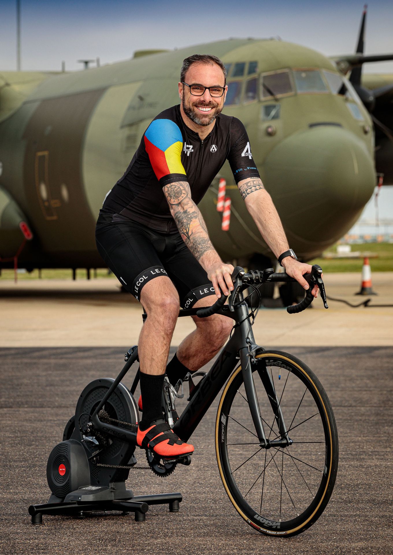 Sergeant Neil King pictured with his bike and turbo trainer, in front of a C130J Hercules.