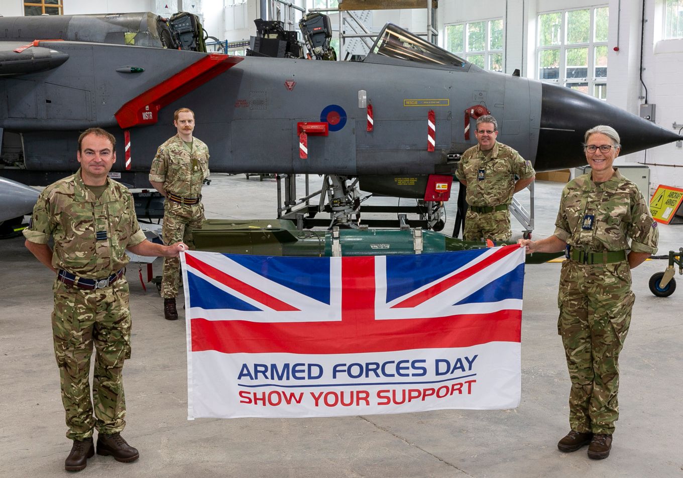 four military personnel holding the Armed Forces Day Flay inside an aircraft hangar