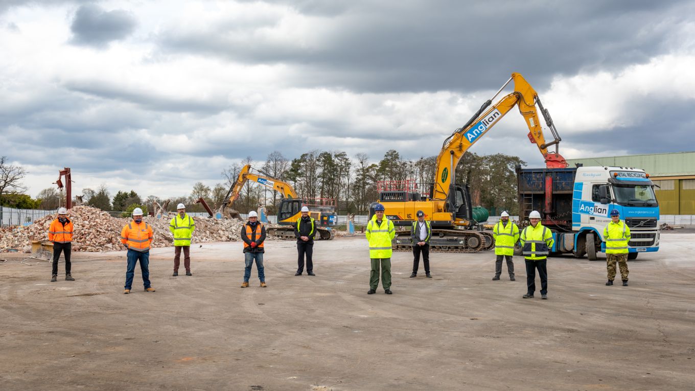Demolition team stand socially distanced in front of demolition site
