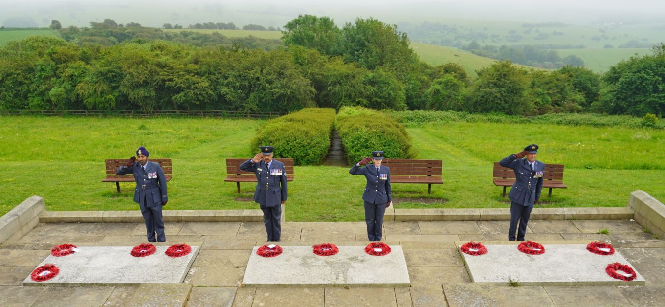 Personnel salute beside the wreaths.