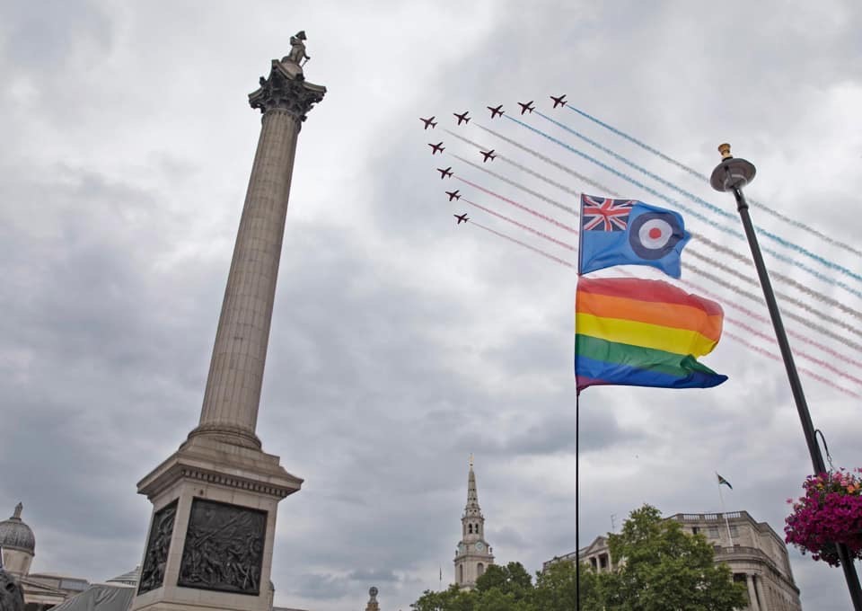 Red Arrows fly over Trafalgar Square and Nelsons Column, with the Pride flag.