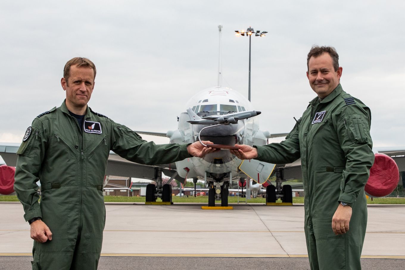 Group Captain Chris Melville and Group Captain Stephen Kilvington hold a trophy together, in-front of a plane. 