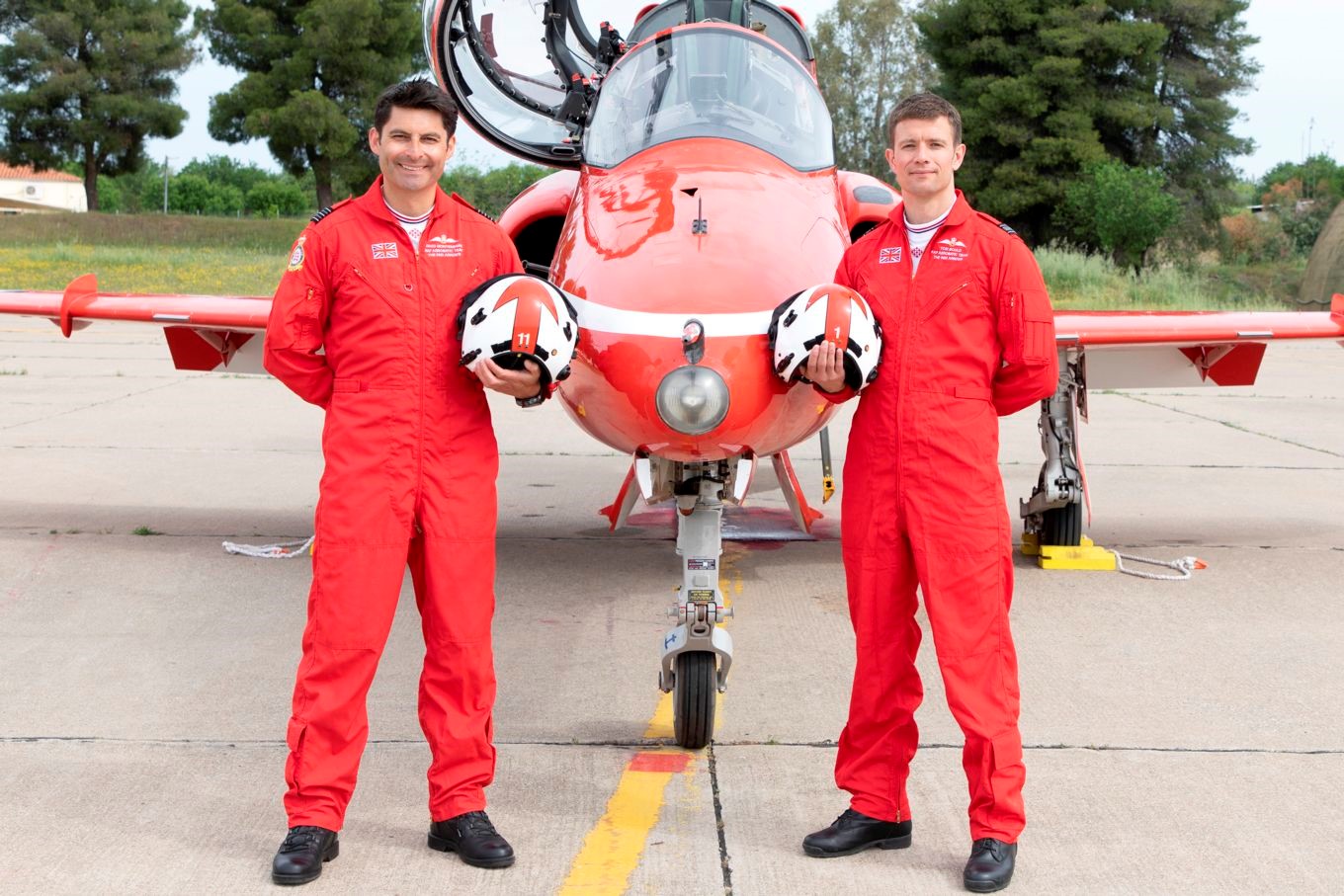 Wing Commander Montenegro and Squadron Leader Boule stand in-front of a Red Arrows Fighter Jet holding their helmets. 
