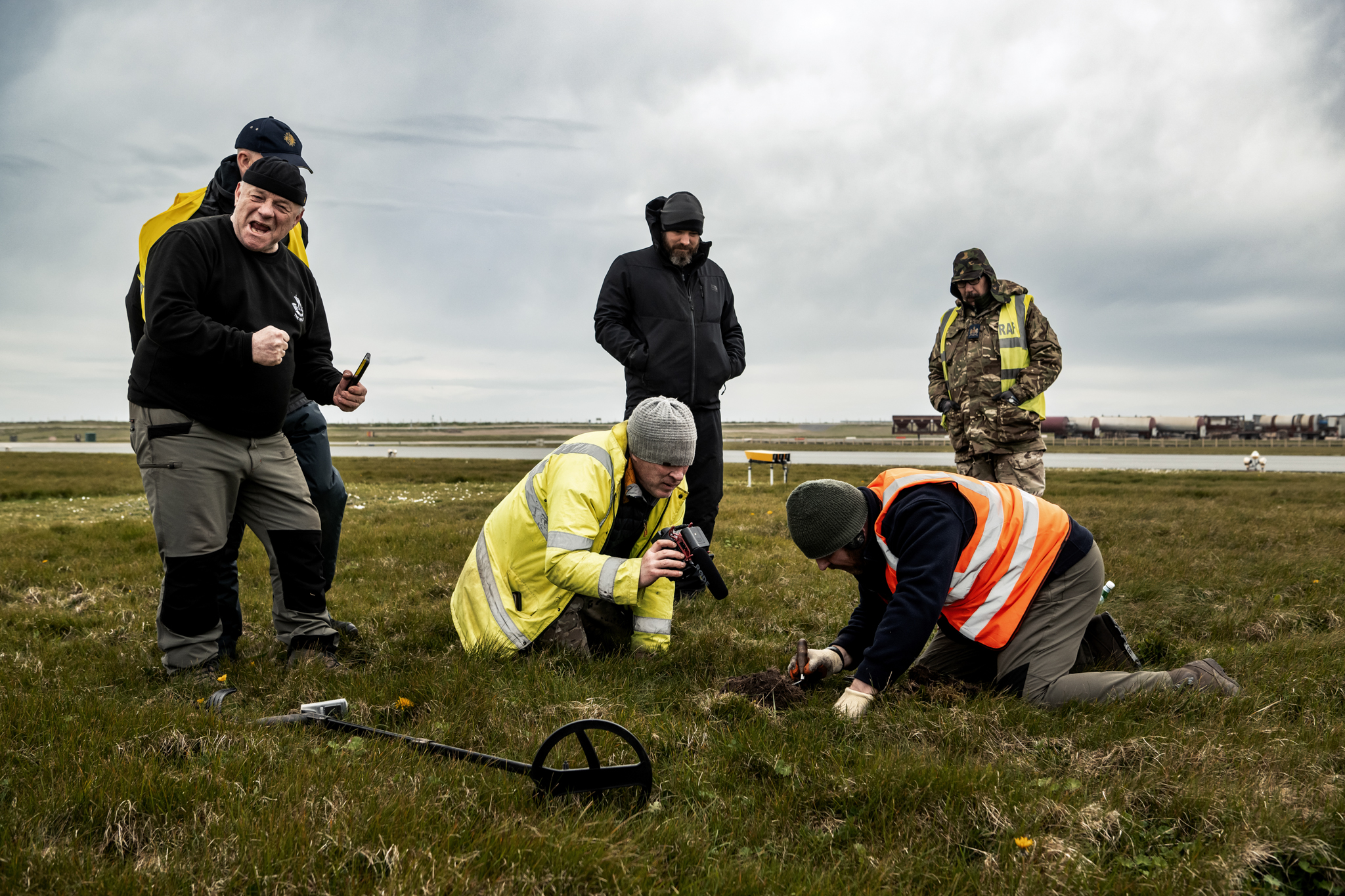 Group of people on-site at the dig, two of them digging and others standing.