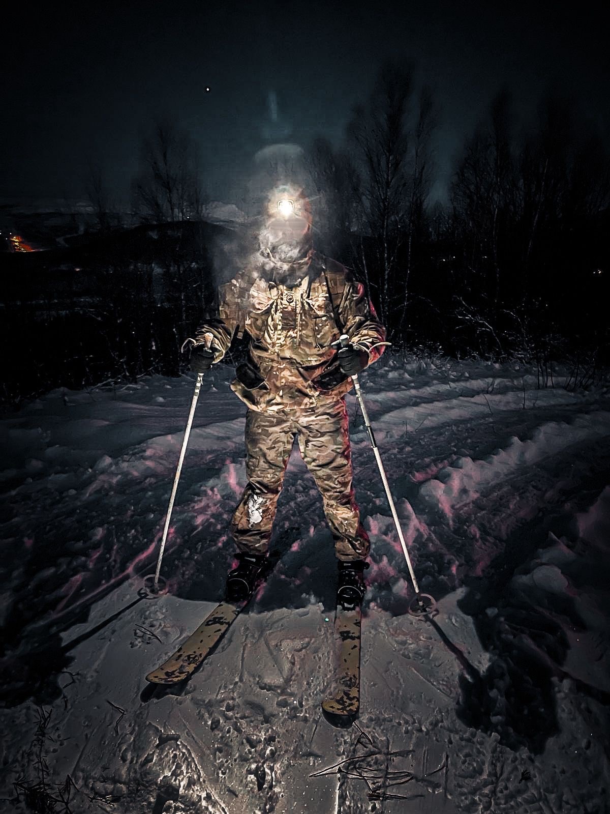 Service person in uniform and on skis, at night, with a head torch on.