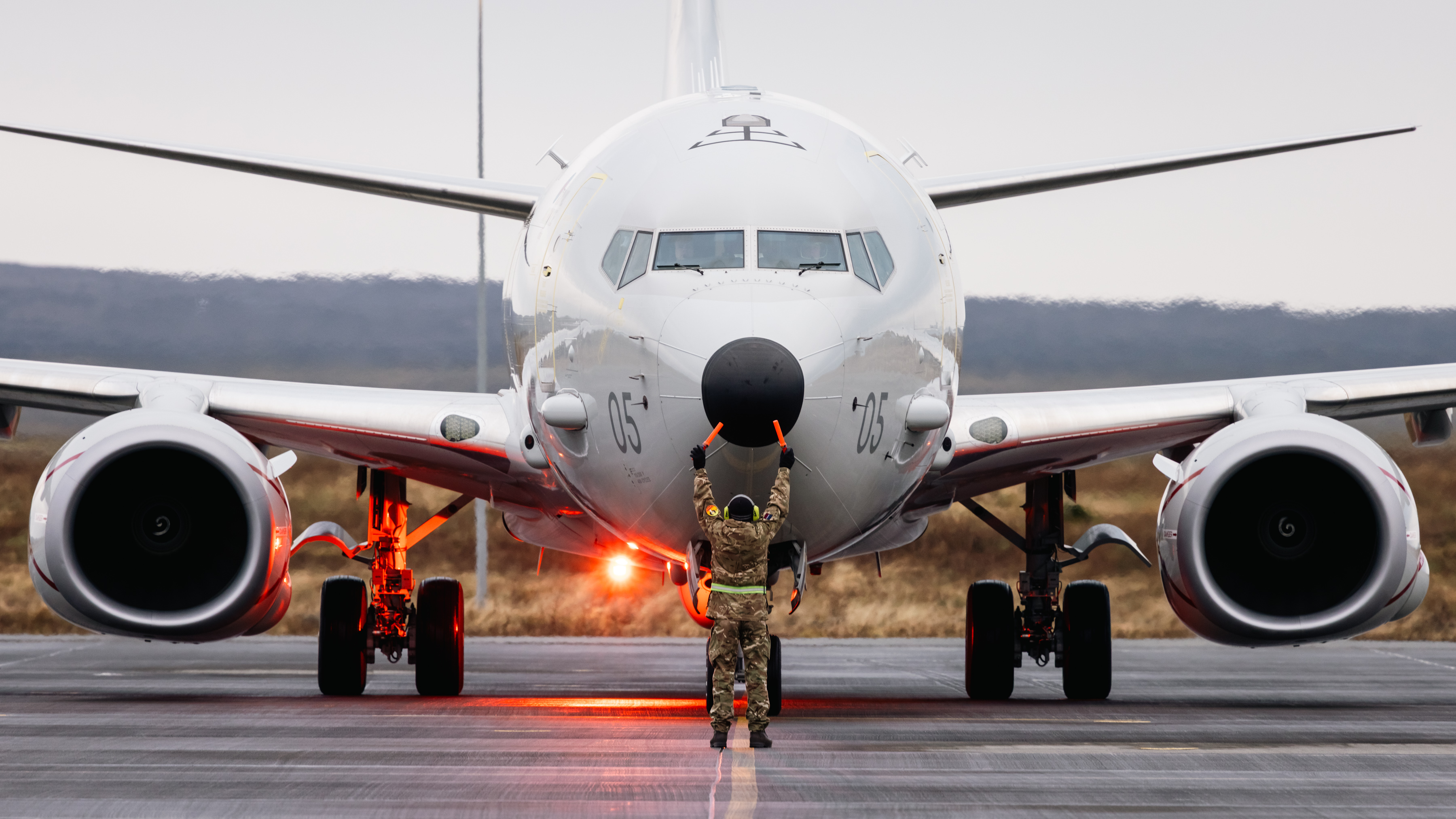 An RAF Poseidon taxiing along a runway, guided by a member of the ground crew.