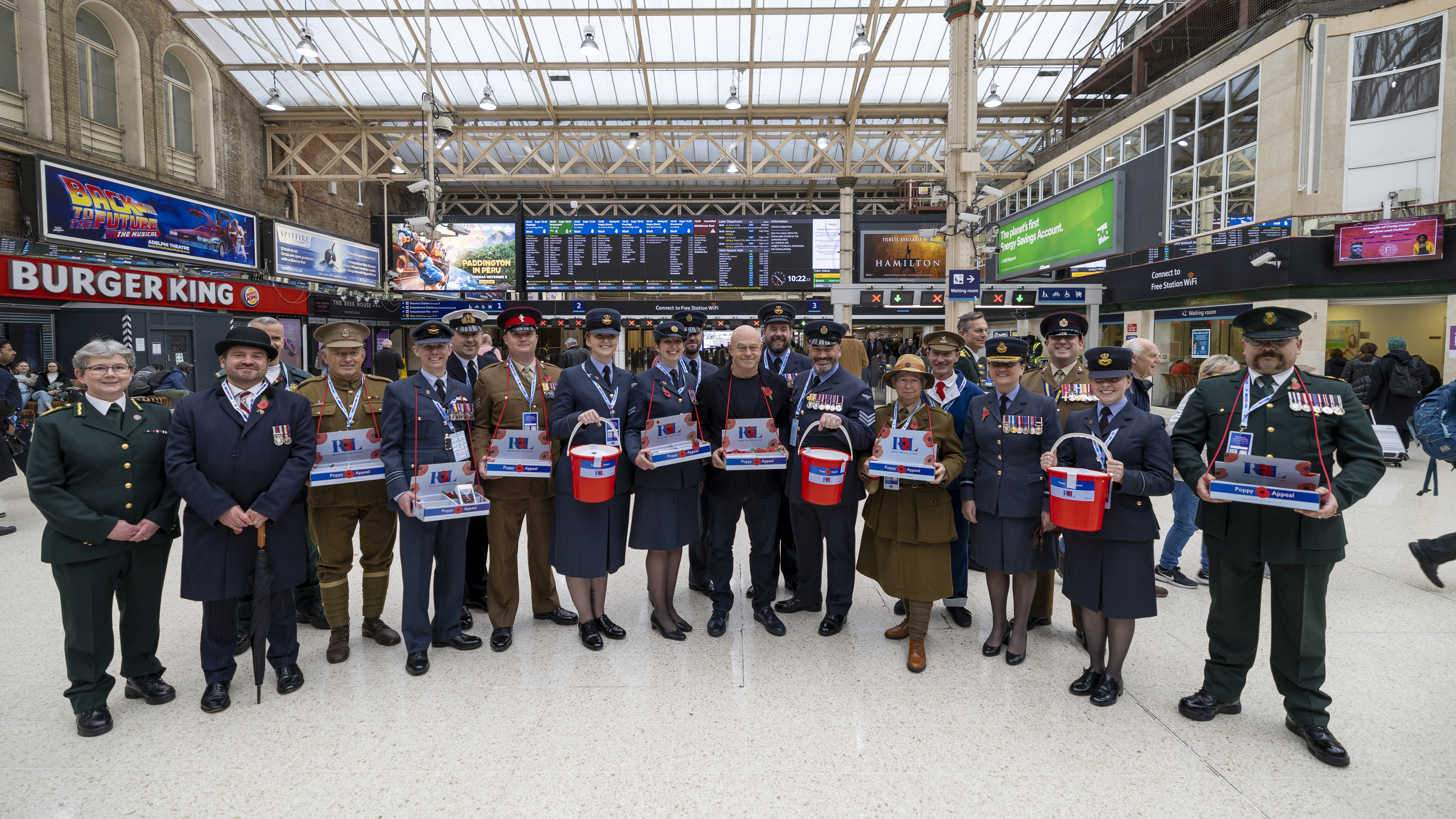 Tri-service personnel hold buckets in train station.