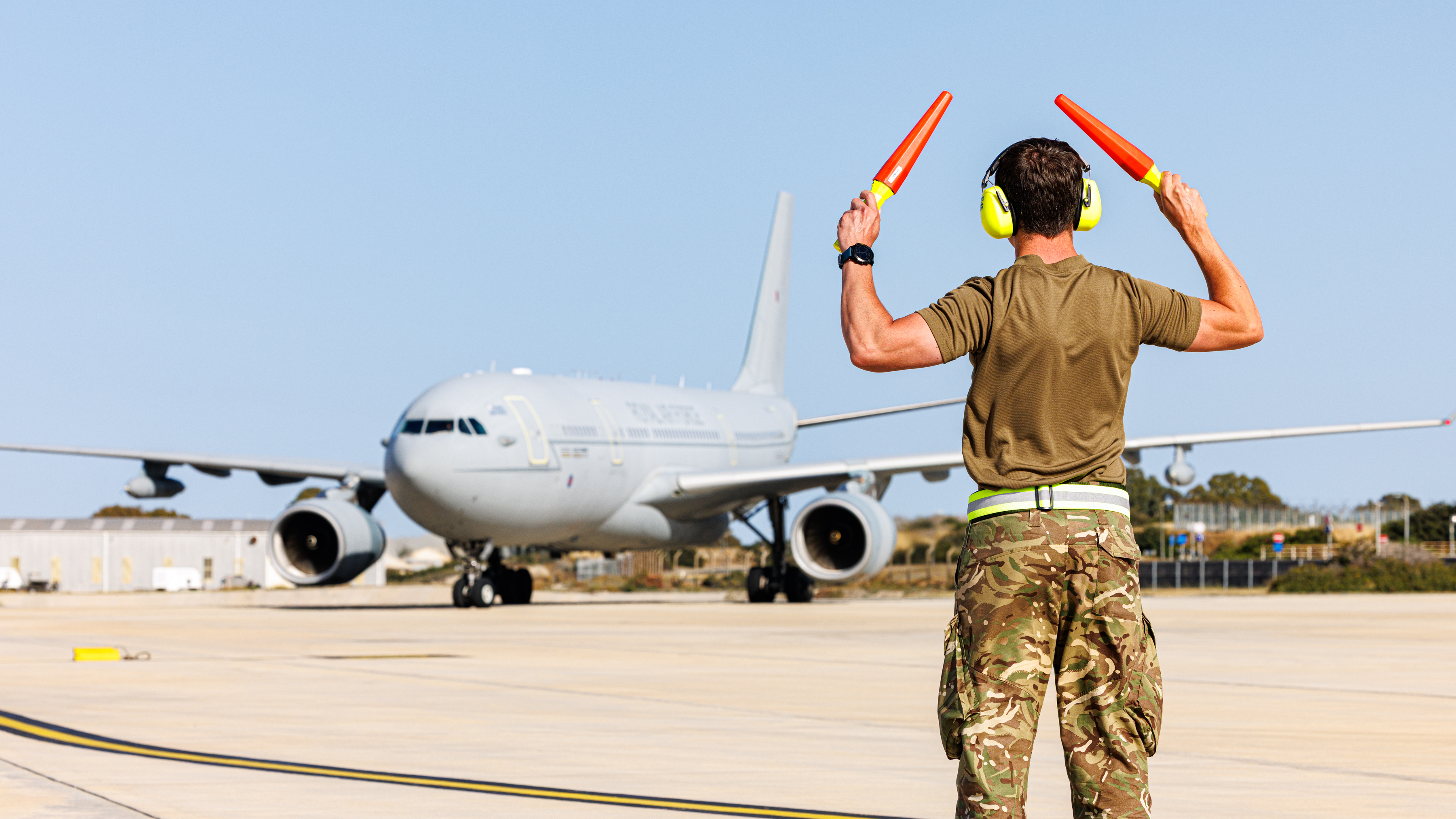 An RAF ground person directing an RAF Voyager across the runway.