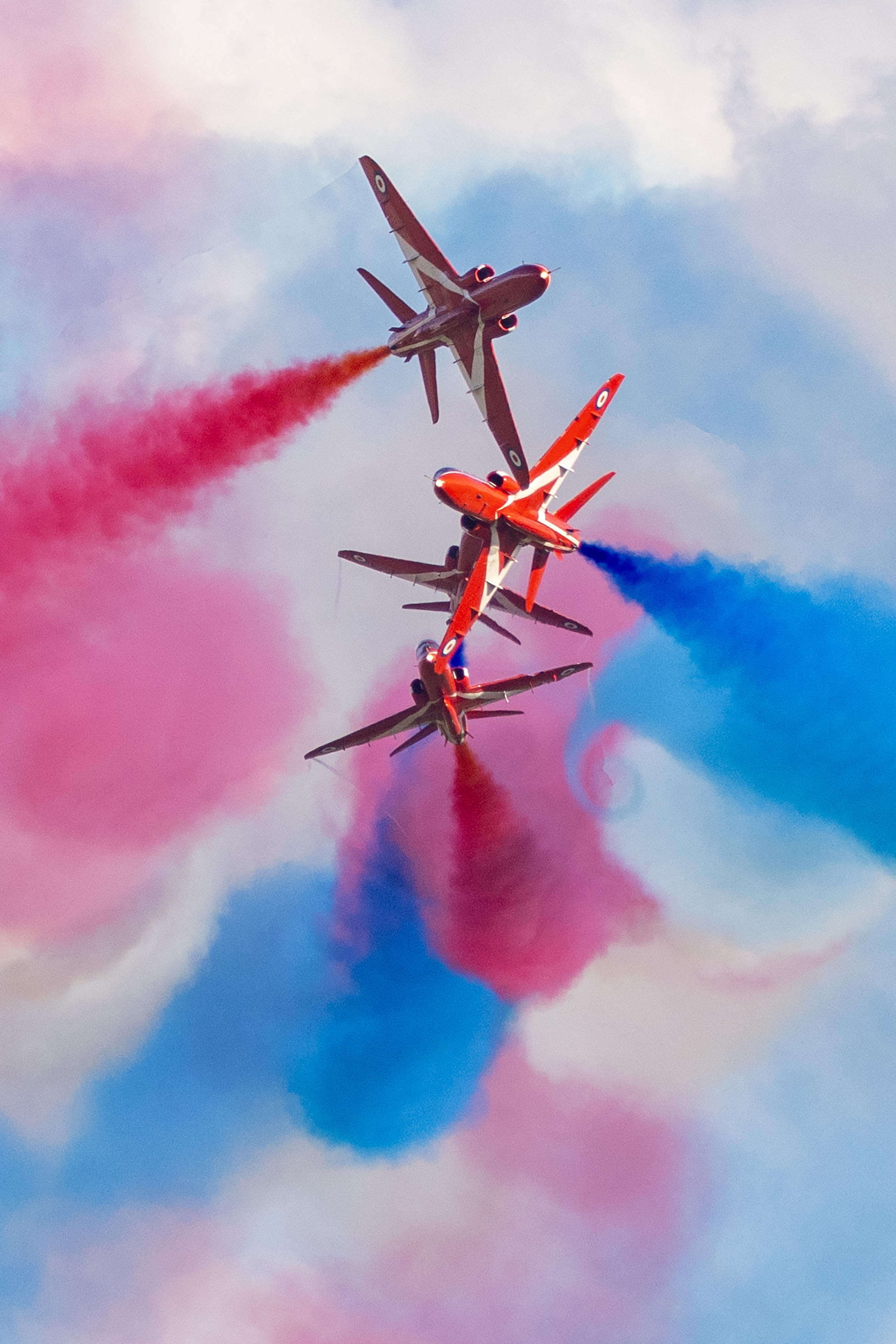 The Red Arrows aircraft performing with red, white, and blue smoke trails.