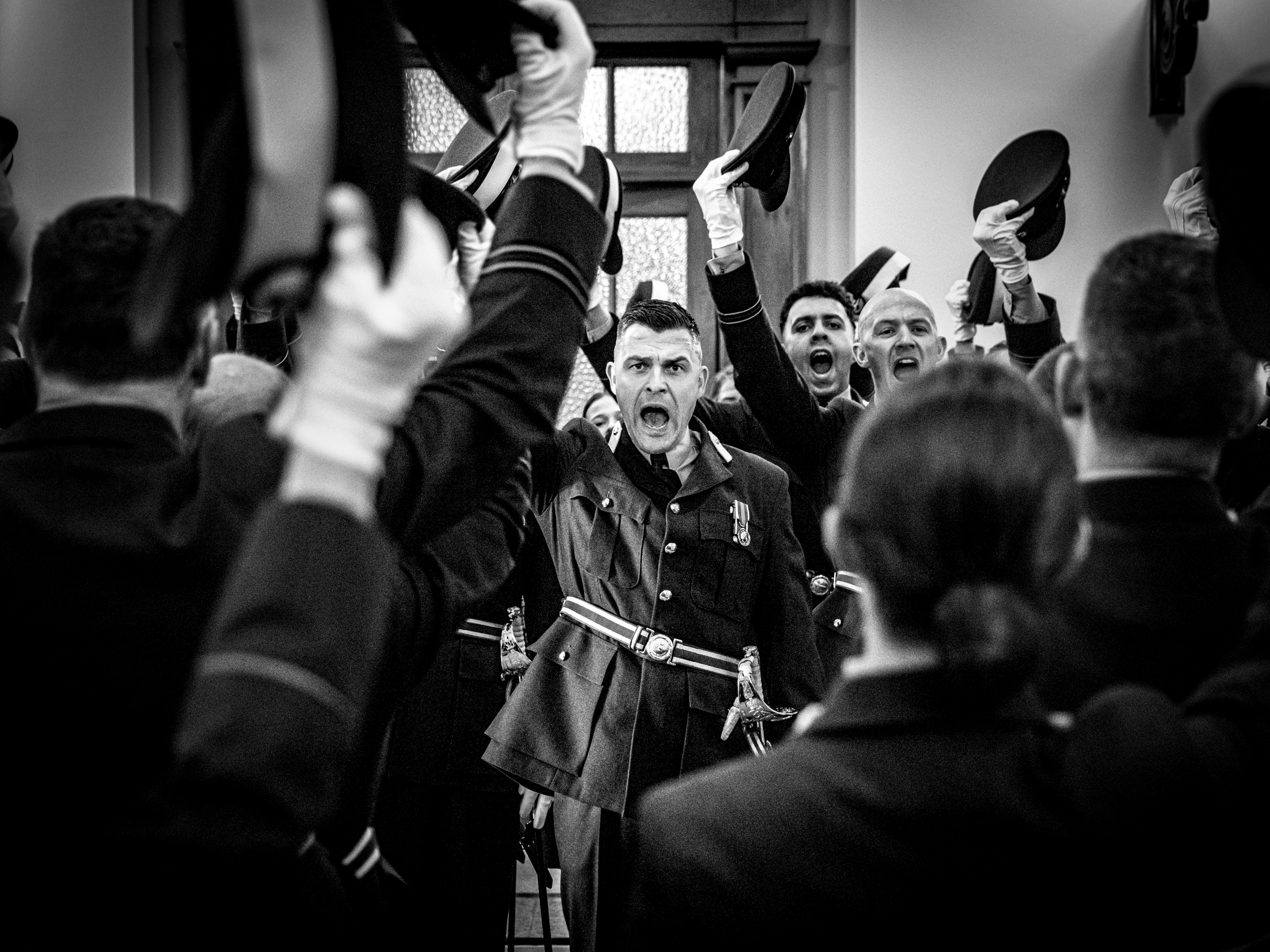 Black and white image of Personnel raising their hats and shouting. 