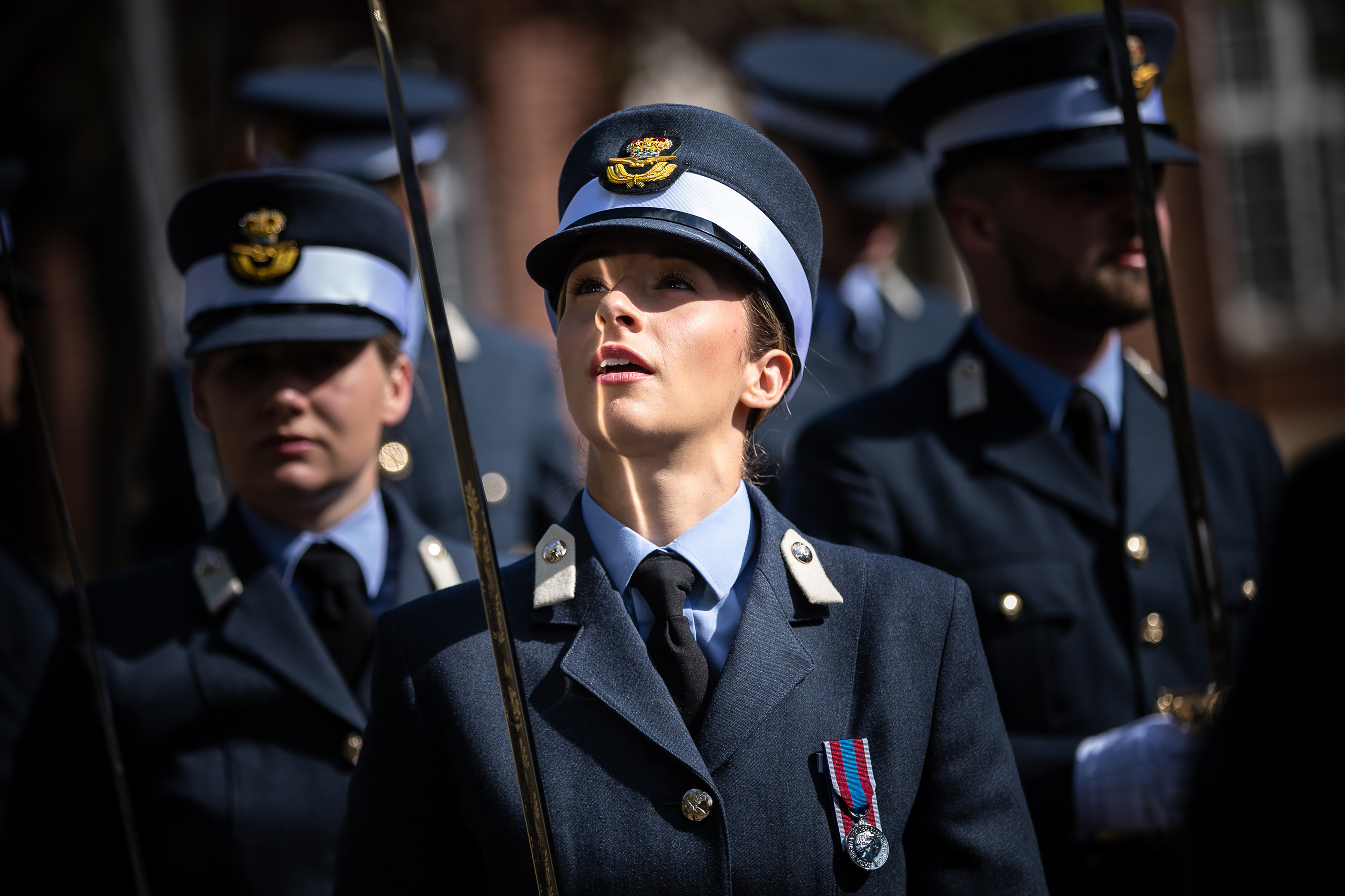 Officer cadet holding their sword up, with it's reflection shining on her face.